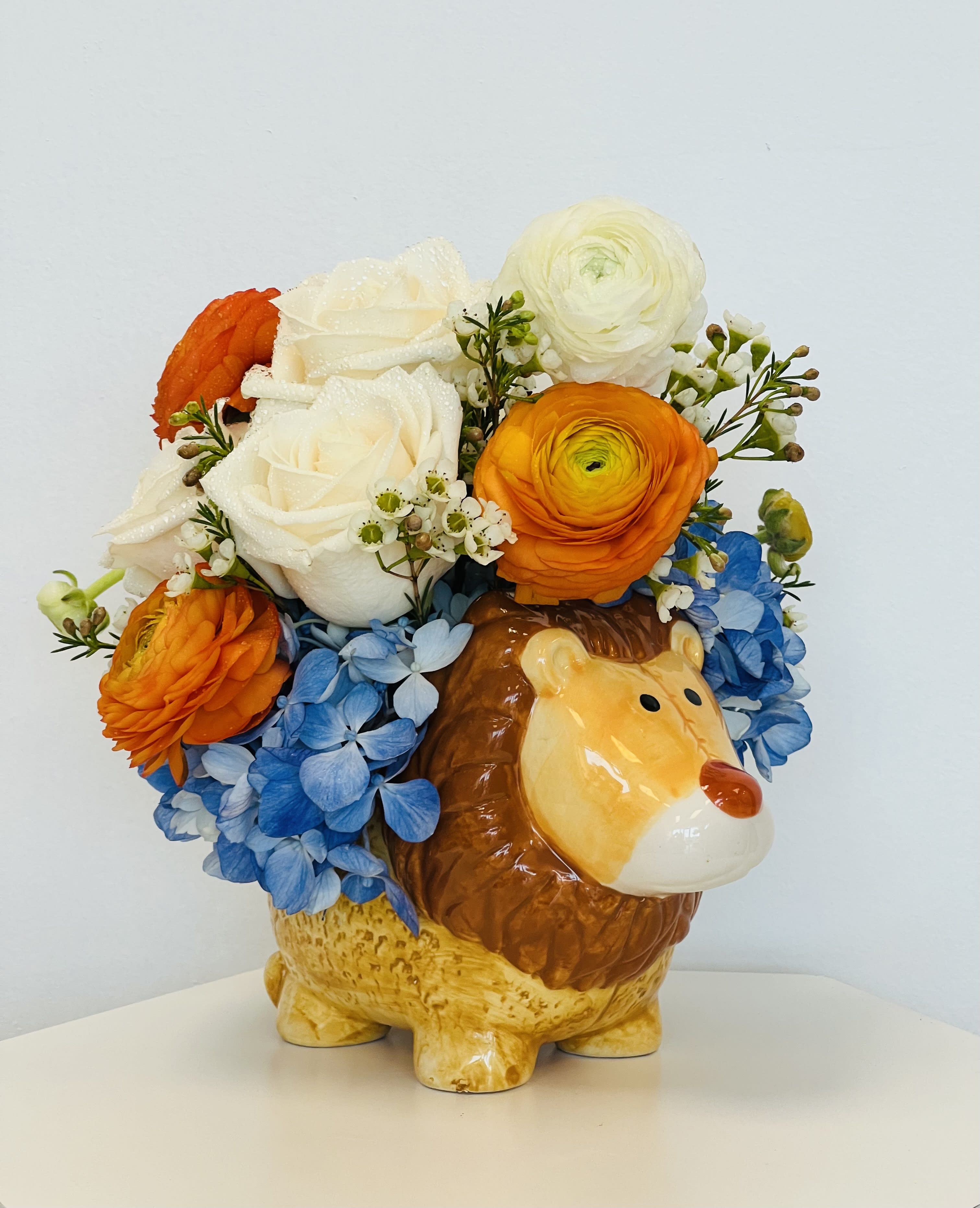 Flower arrangement in a ceramic lion planter with blue hydrangeas and orange and white blooms