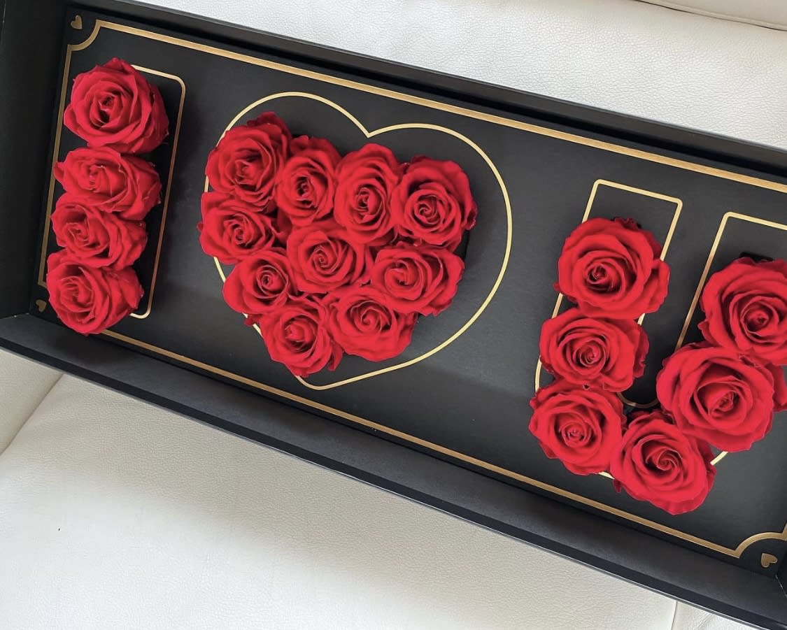 Red roses arranged in a black box with gold heart and letter outlines