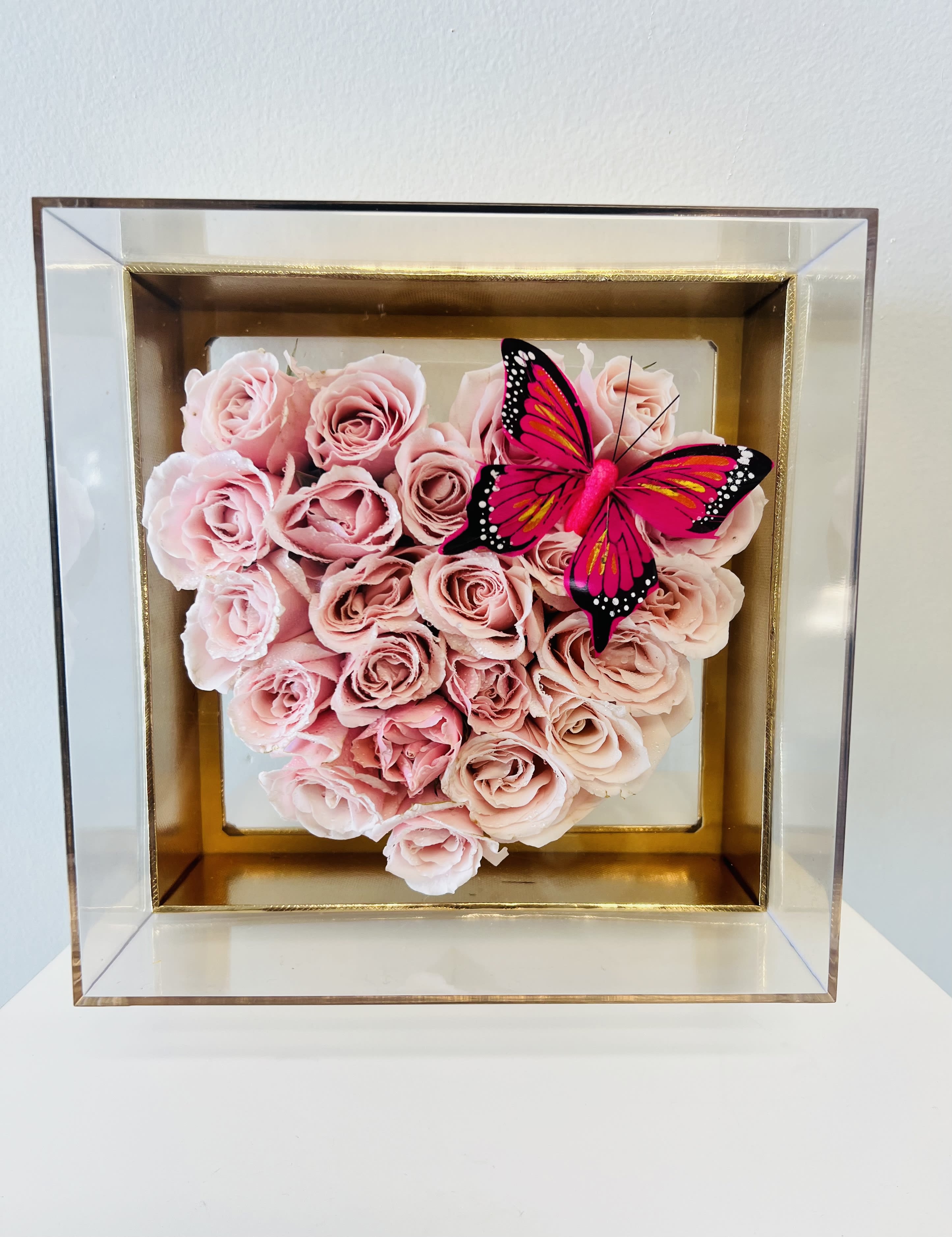 Pink roses arranged in a square shadow box with a butterfly accent