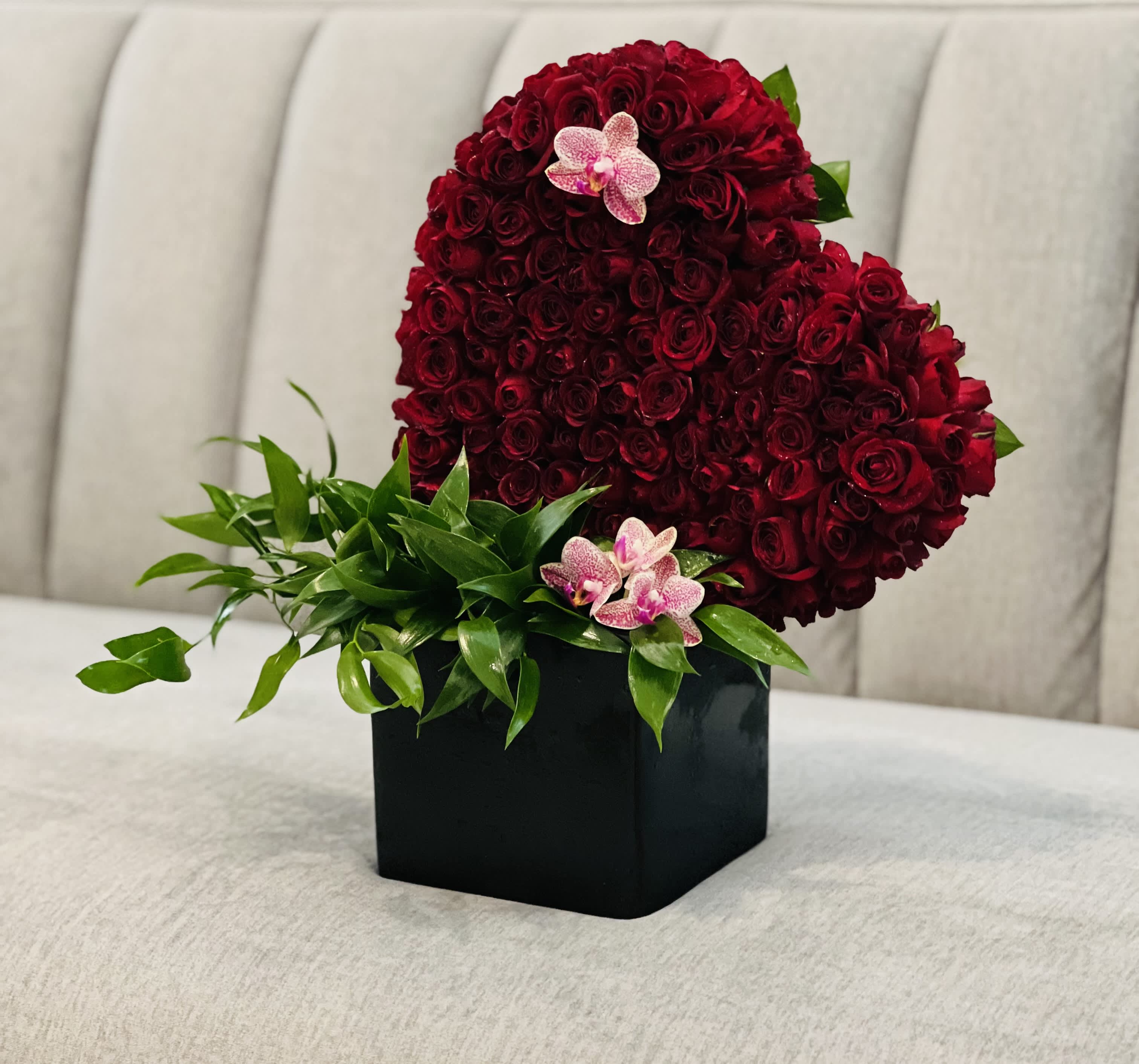 Heart-shaped red rose arrangement in a black box with pink orchids