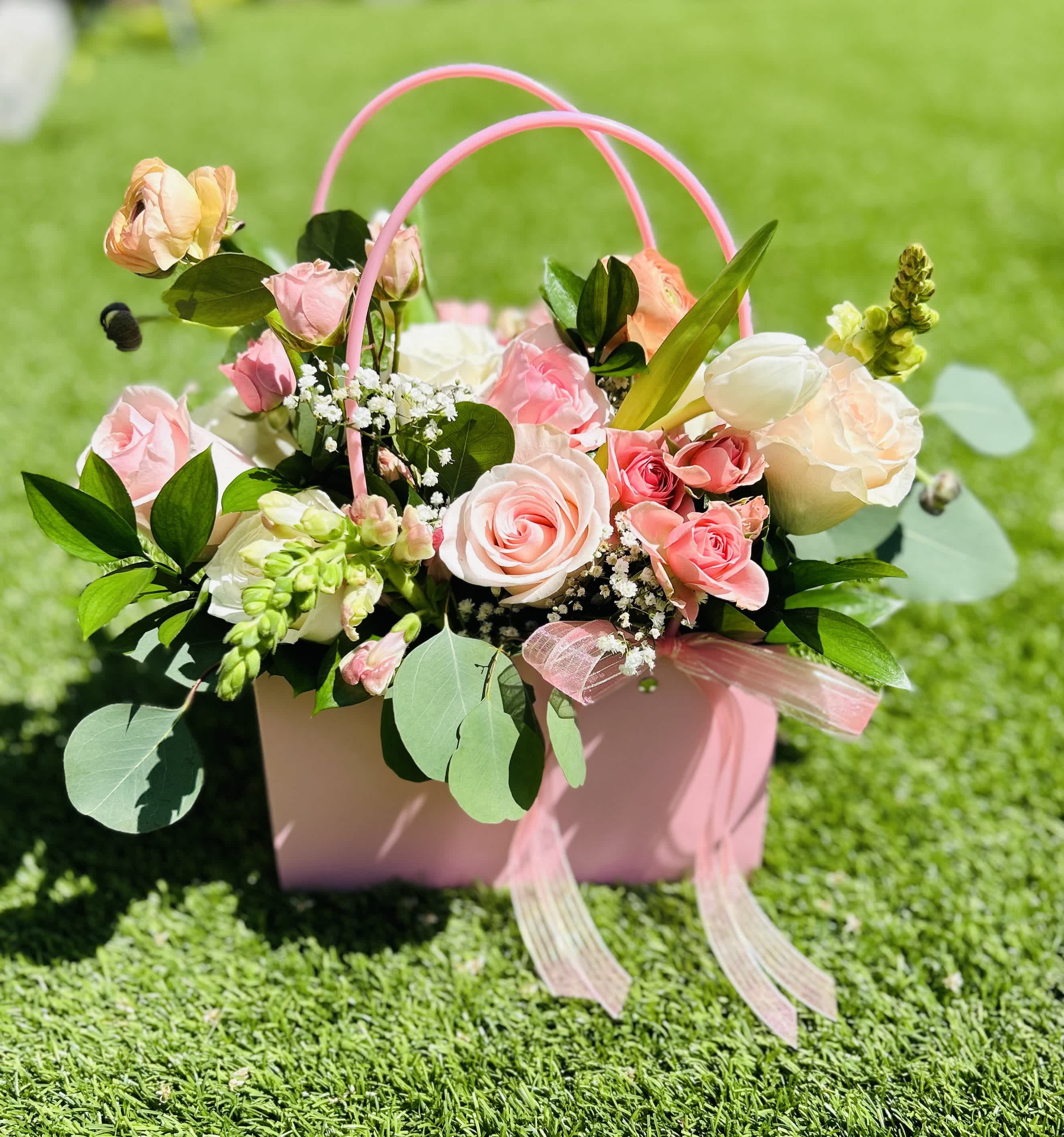 Pink and white roses in a pink handled gift box on grass