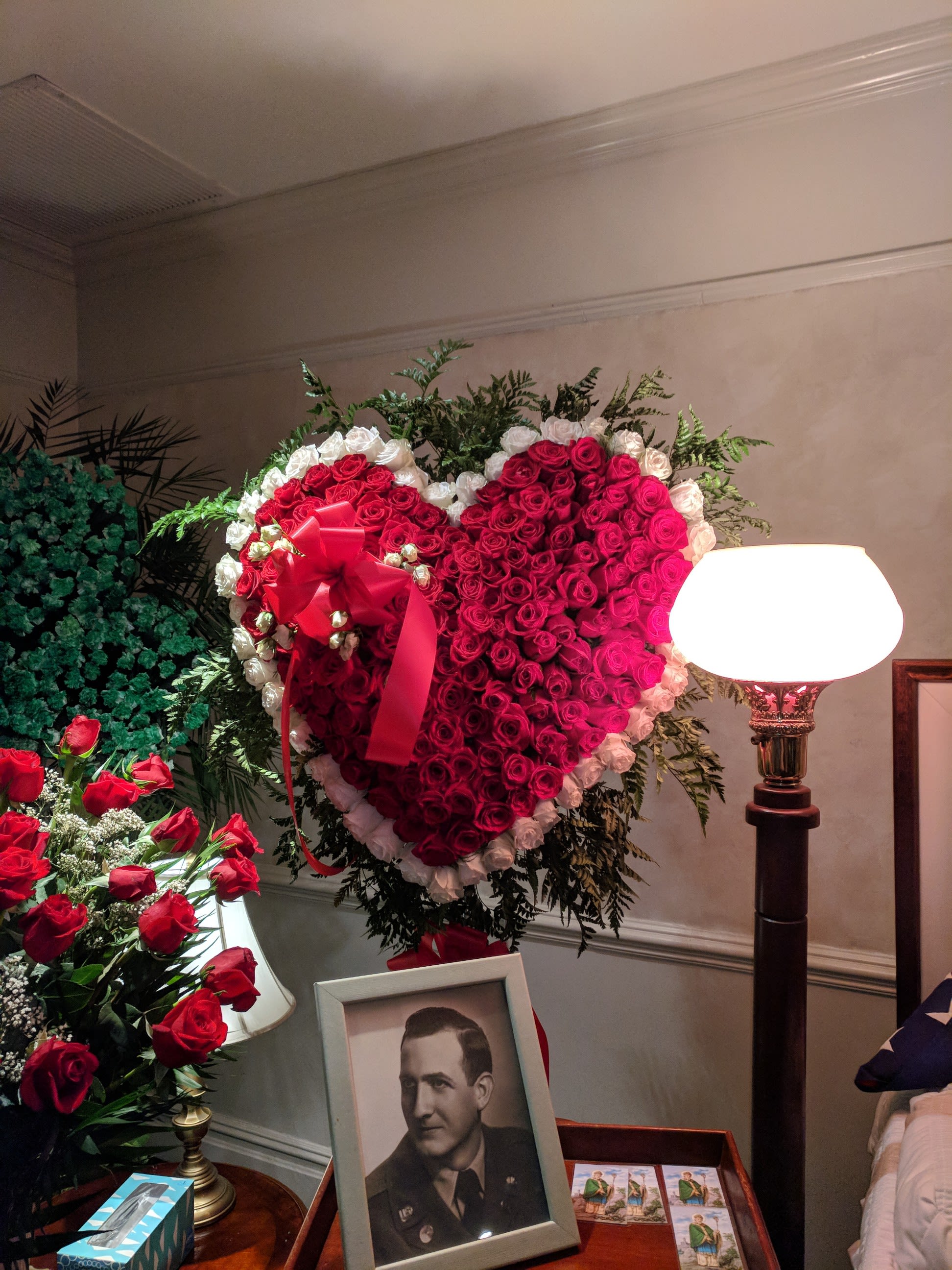 Heart-shaped red rose wreath with a red ribbon beside a framed portrait