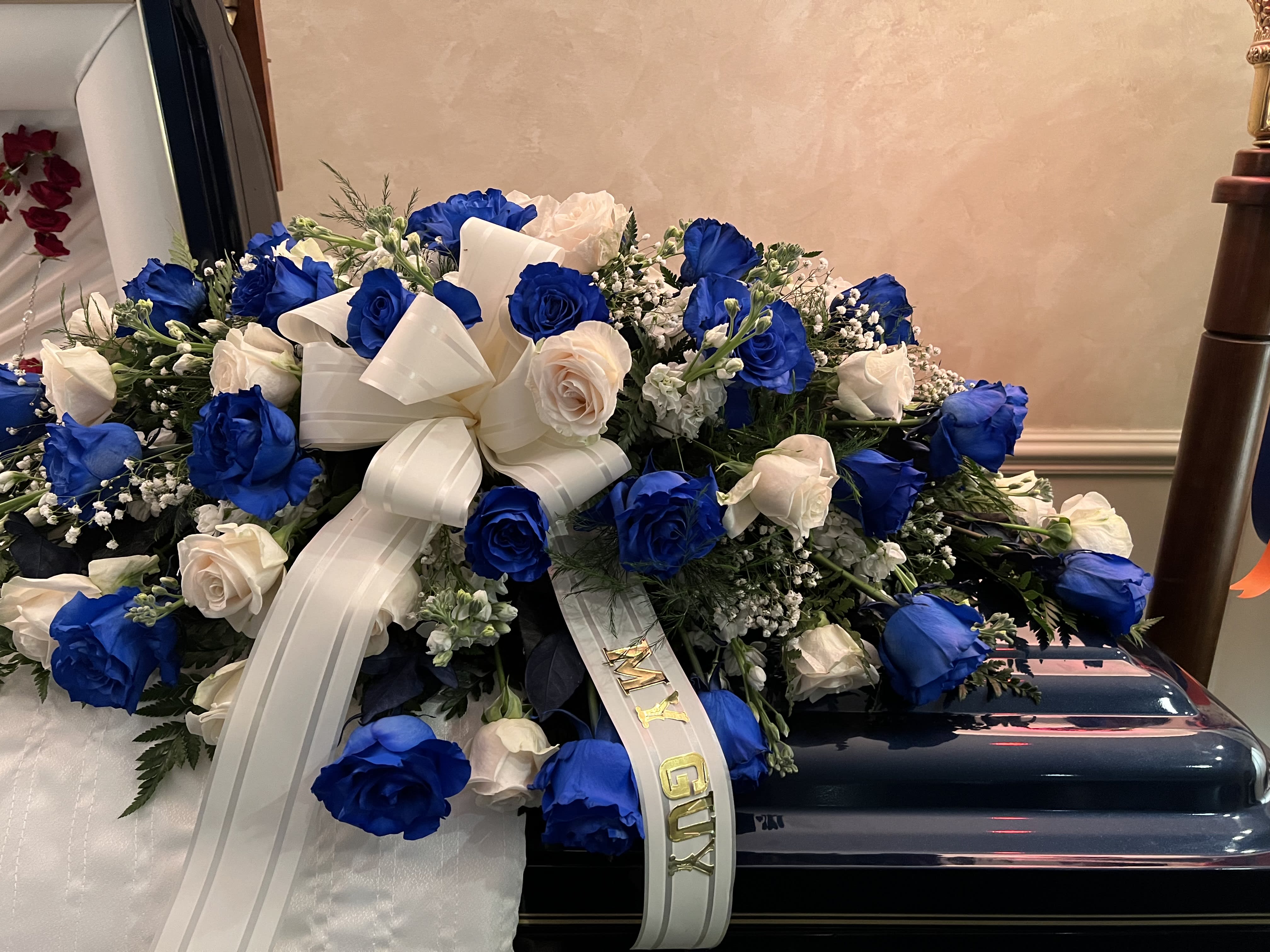 Blue and white rose arrangement with a ribbon on a casket