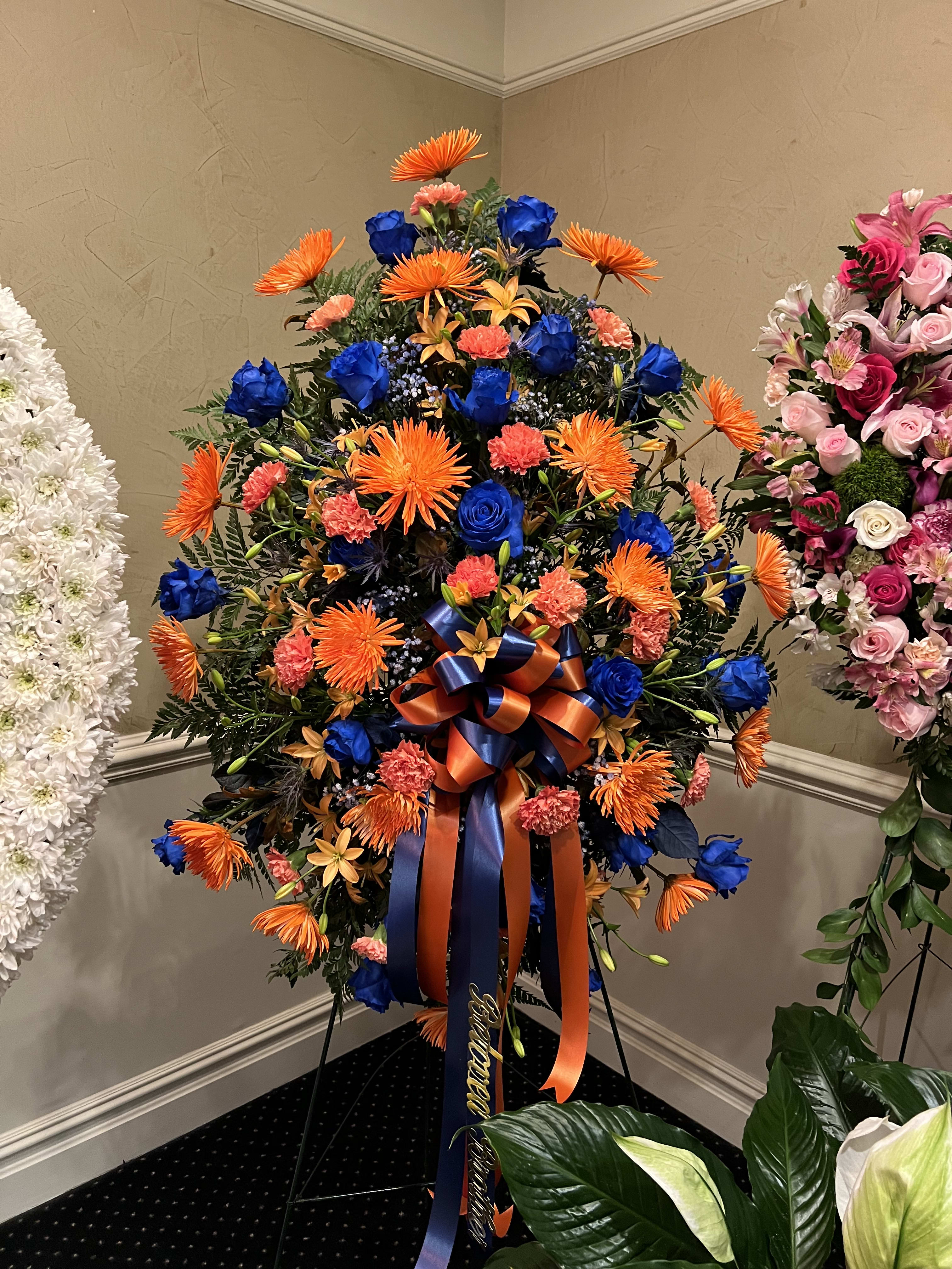 Standing floral wreath with orange, blue, and coral blooms on an easel
