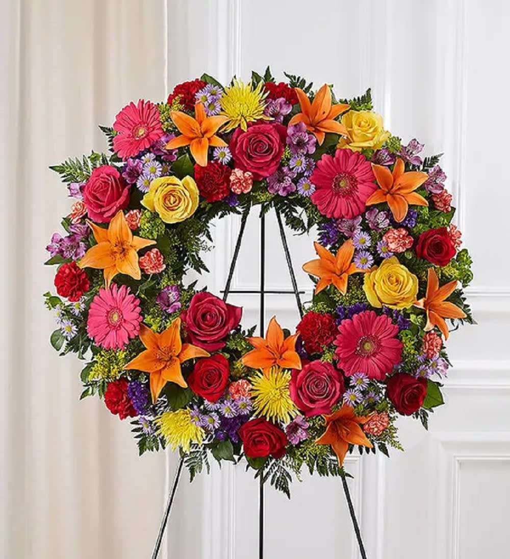 Large circular funeral wreath with roses, lilies, and daisies on an easel