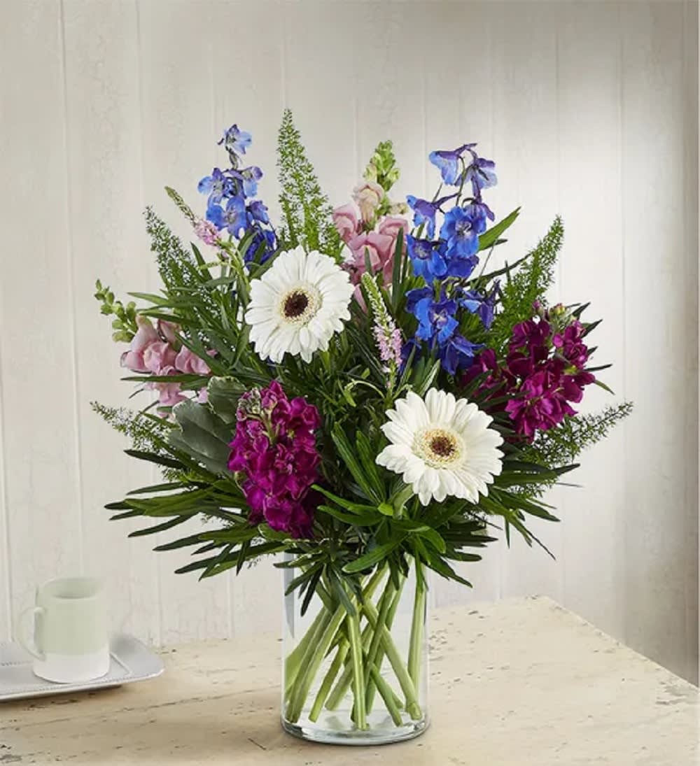 Mixed bouquet with white daisies, blue and pink flowers in a clear glass vase