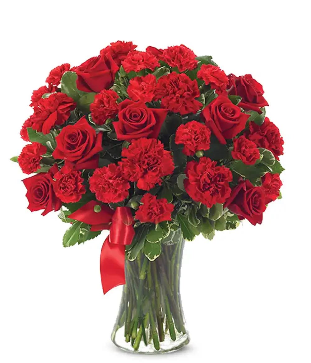 Red roses and carnations arranged in a clear glass vase with a red ribbon