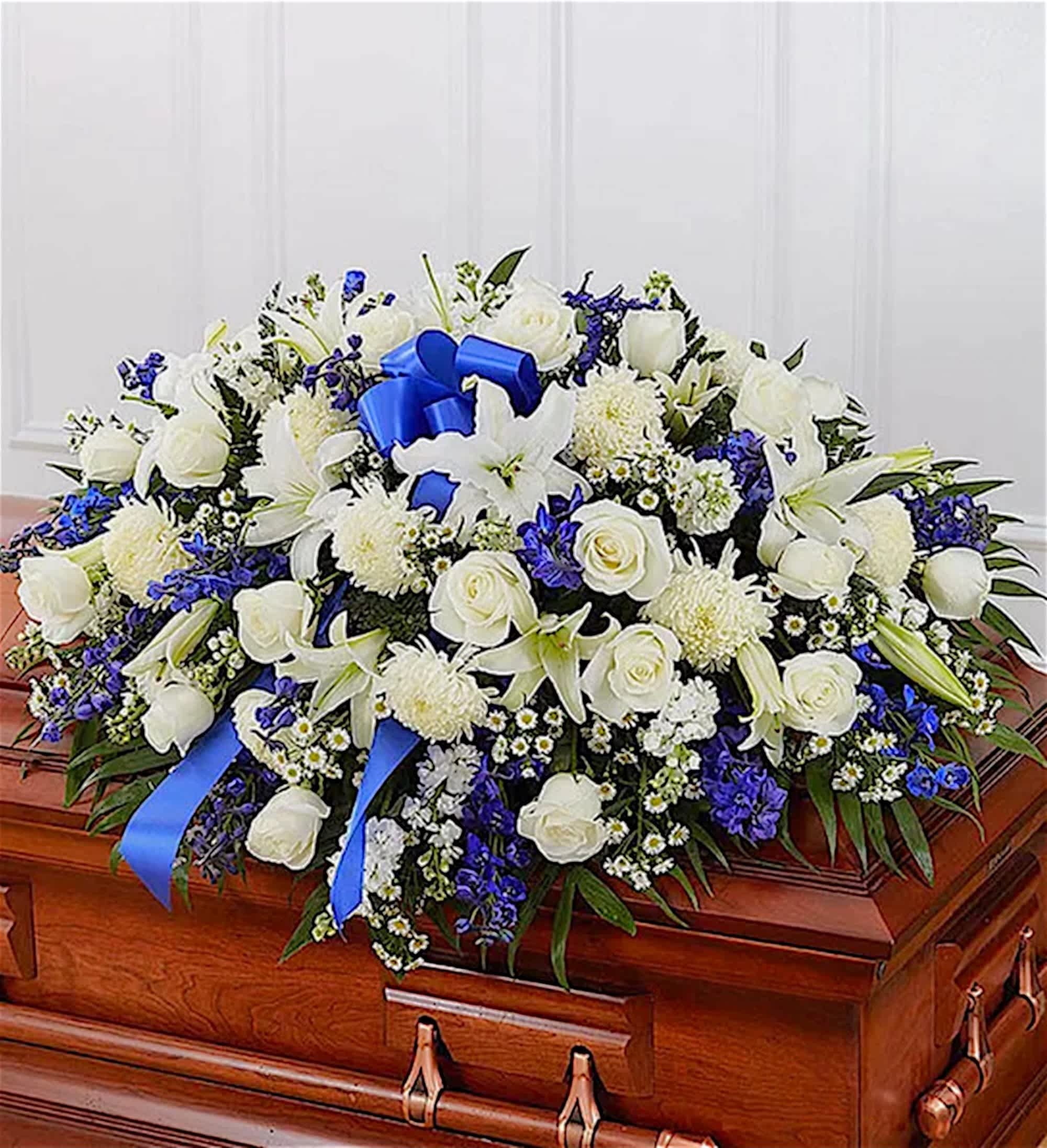 Blue and White Mixed Half Casket Cover - Honor a life so beautifully lived with a proud display of blue and white blooms. Our half casket cover, crafted with care and artistry with blue delphinium, white roses, and accented with a blue satin ribbon, is an unforgettable way to commemorate a lifetime of loving devotion.  DETAILS Half casket cover arrangement of white roses, hybrid lilies, football mums, monte casino and stock, blue delphinium and emerald; accented with a blue satin ribbon. Traditionally sent by the immediate family to the funeral home.  Orientation: All-Around *If you would like to add a ribbon with a sentiment for an additional $10 each. Item #NF-1013  FLORIST-TO-DOOR Same day flower delivery on most orders placed online by 12 pm or 10 am on weekends PST.  BLOOM DETAILS Roses Stock Delphinium Football Chrysanthemums Hybrid Lilies Montecasino Spray Greenery  The Standard Arrangement is approx. 18"H x 38"L x 28"D (SHOWN) The Deluxe Arrangement is approx. 18"H x 38"L x 28"D The Premium Arrangement is approx. 18"H x 38"L x 28"D  How to place an order?  1. You can place an order directly on this secure website. OR 2. You can call in your order by dialing: (323) 262 - 9238 OR 3. You can visit our store (appointment recommended 323.262.9238)  NINFA'S FLOWERS 2405 WHITTIER BLVD. LOS ANGELES, CA. 90023