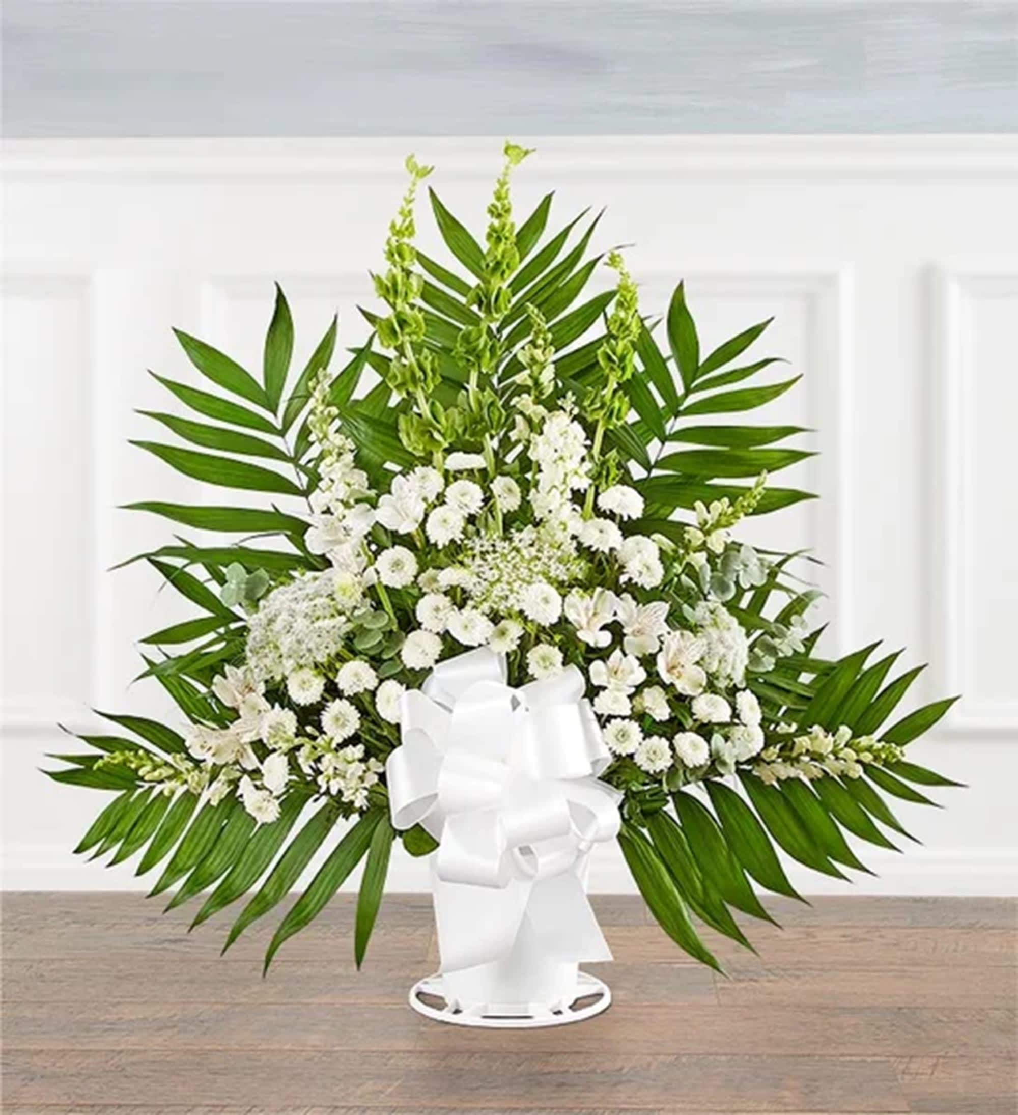 White floral standing spray with palm fronds and a white ribbon bow