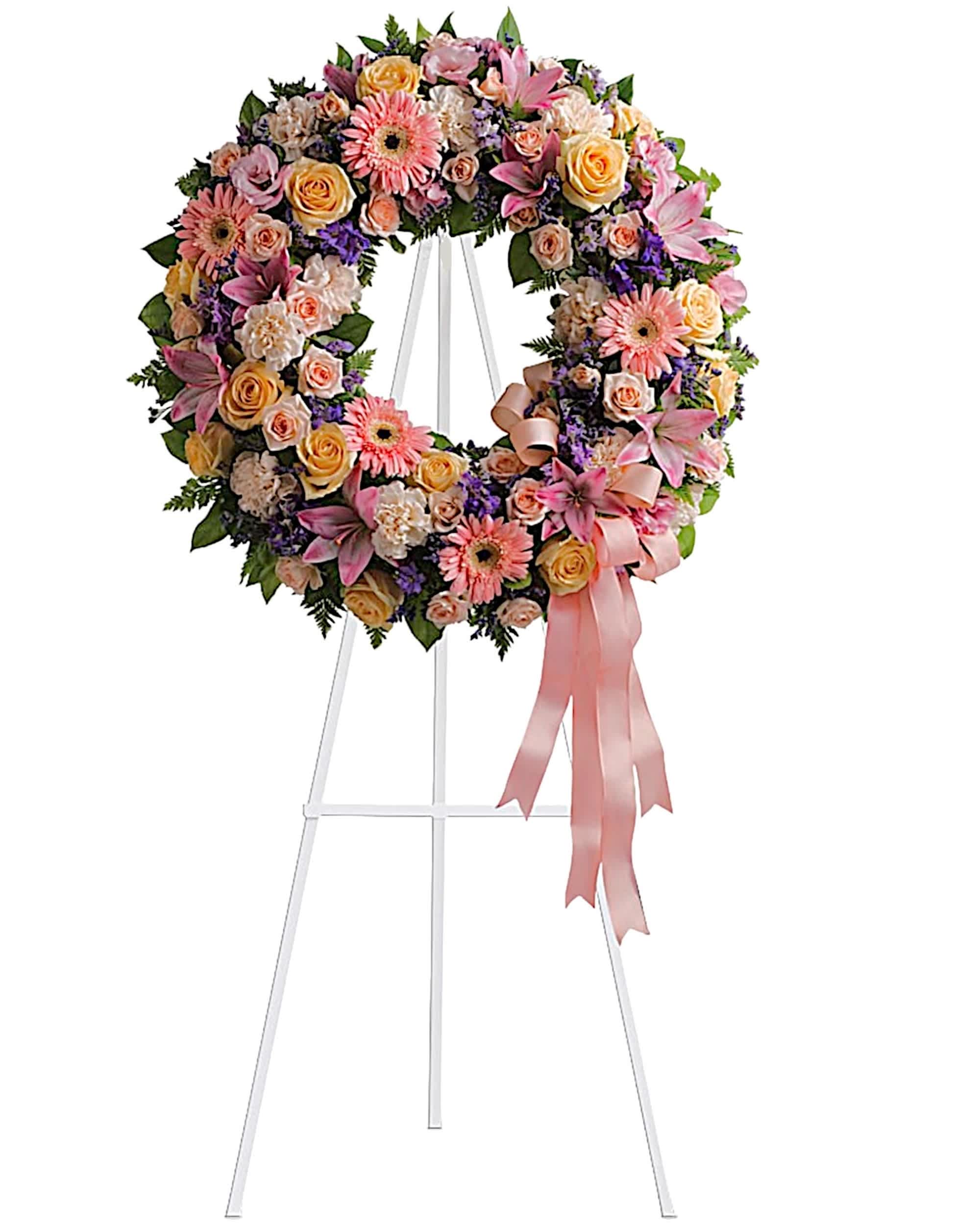 Pink and peach floral wreath on a white stand with a ribbon bow