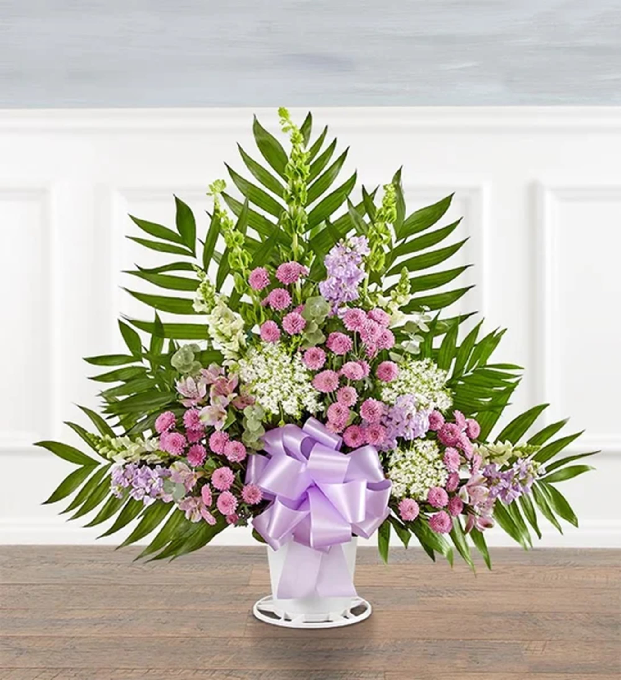 Standing floral spray with pink and lavender blooms in a white vase with a purple bow