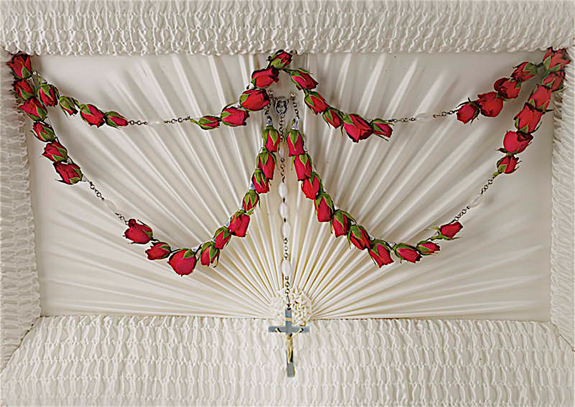 White casket spray with red rose garlands and a cross pendant