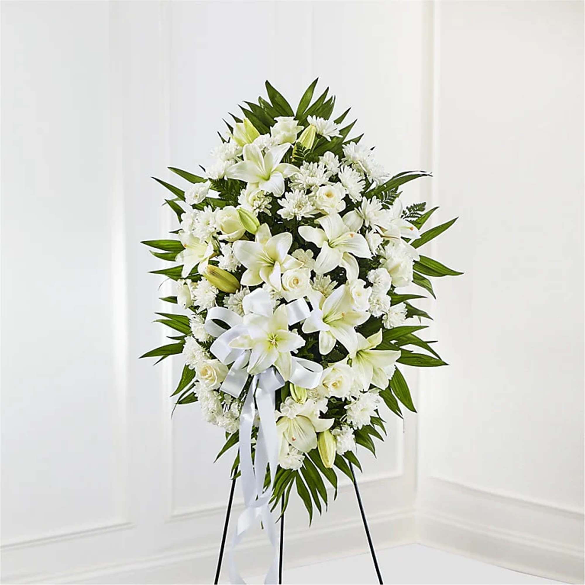 White floral standing spray on a black easel with a ribbon bow