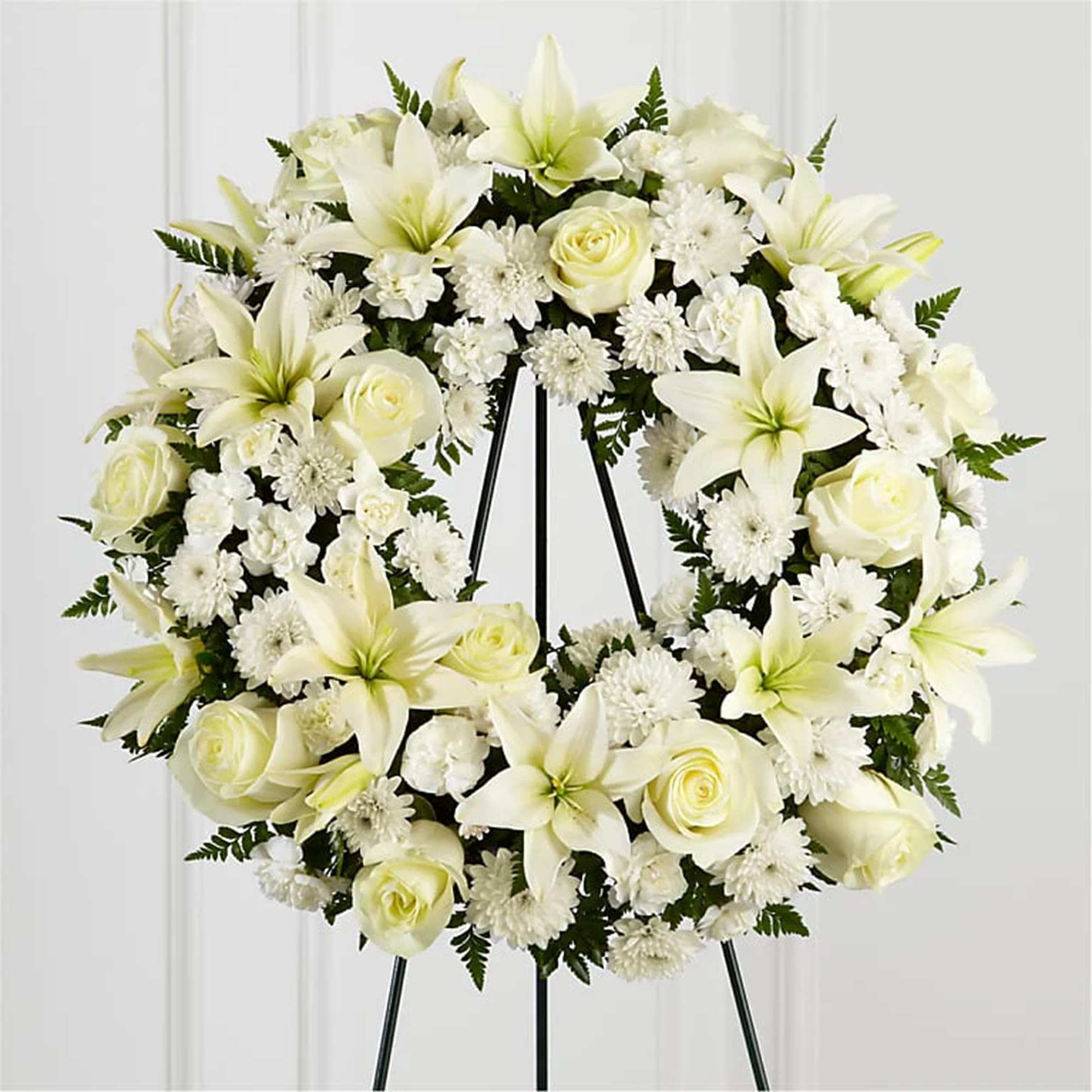 White floral wreath on a black stand with roses and lilies