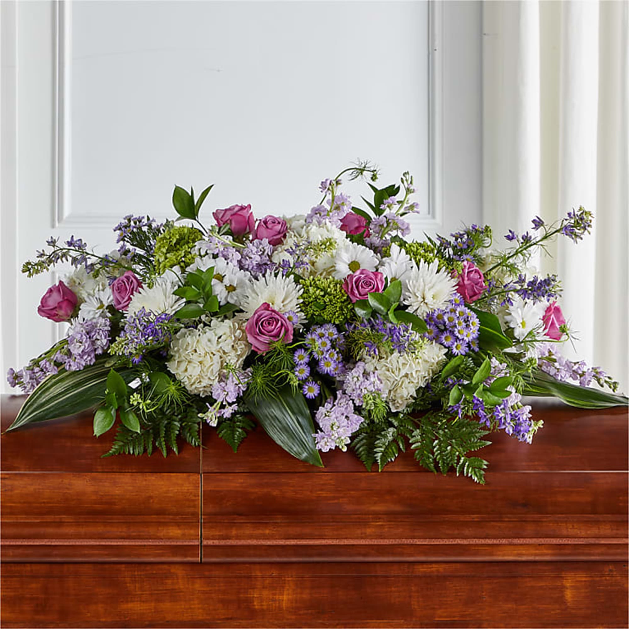 Large floral casket spray with pink roses, white daisies, and purple blooms
