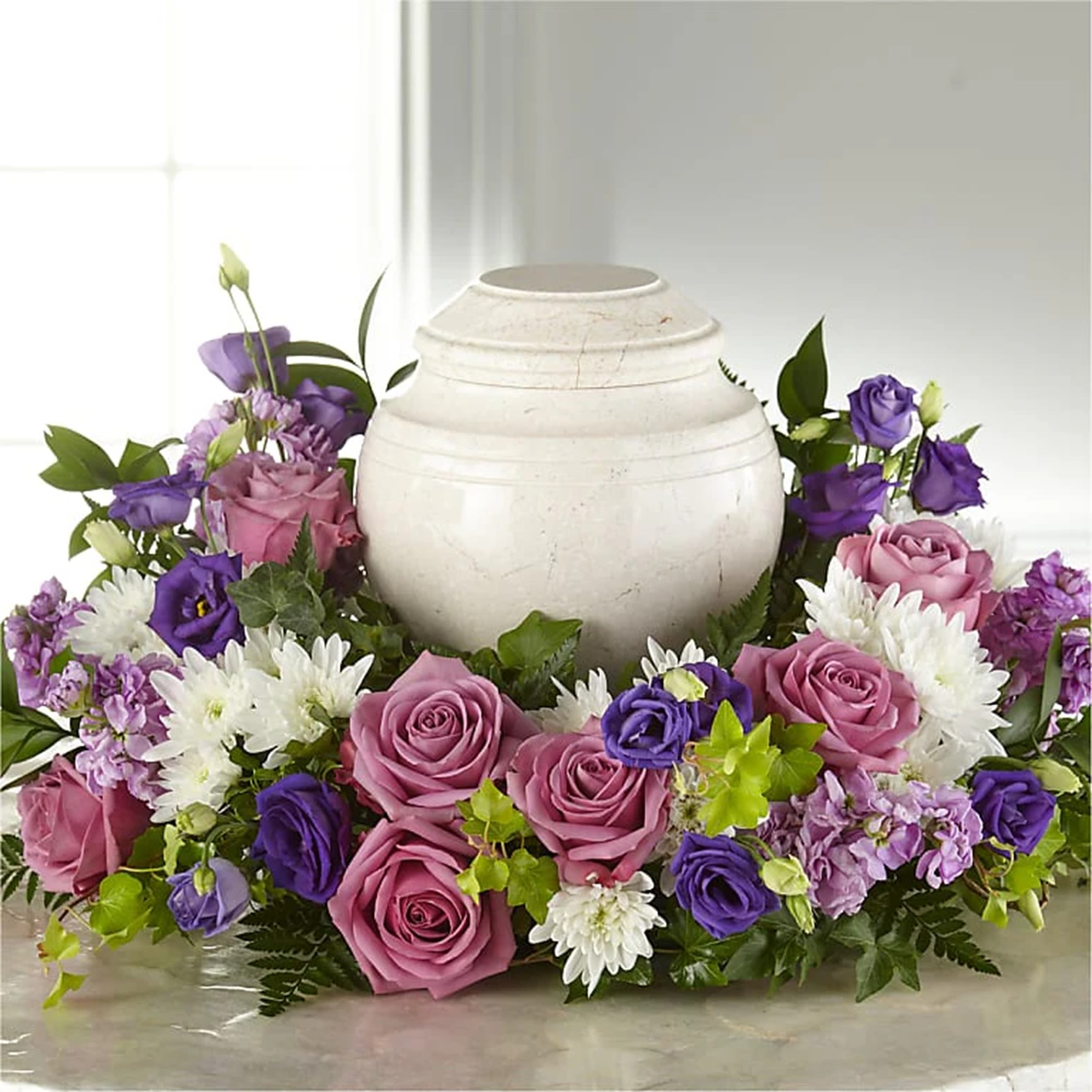 Purple and pink roses arranged around a white urn