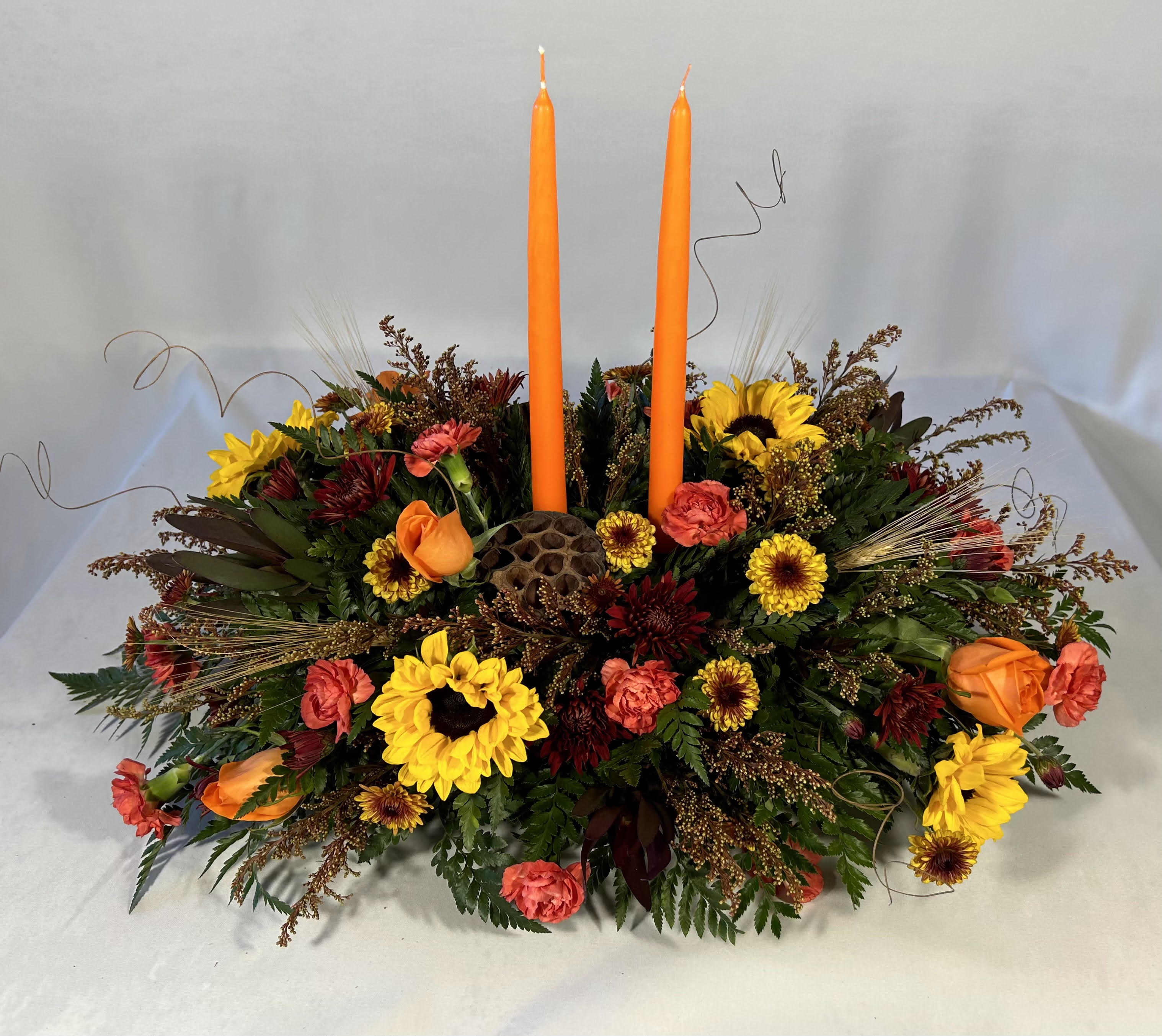 Low floral centerpiece with two orange taper candles and mixed autumn blooms