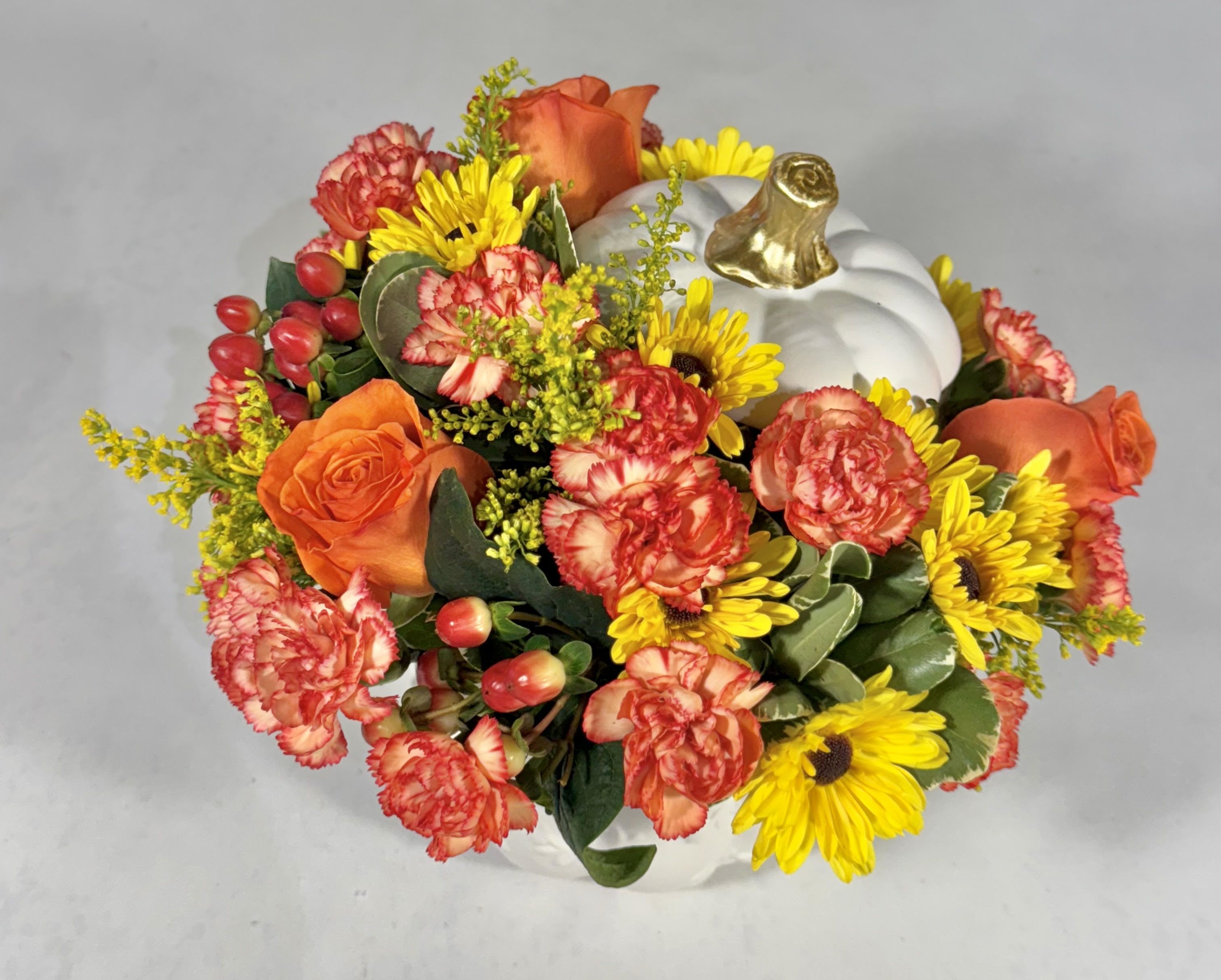 Orange roses and yellow daisies arranged in a white pumpkin container