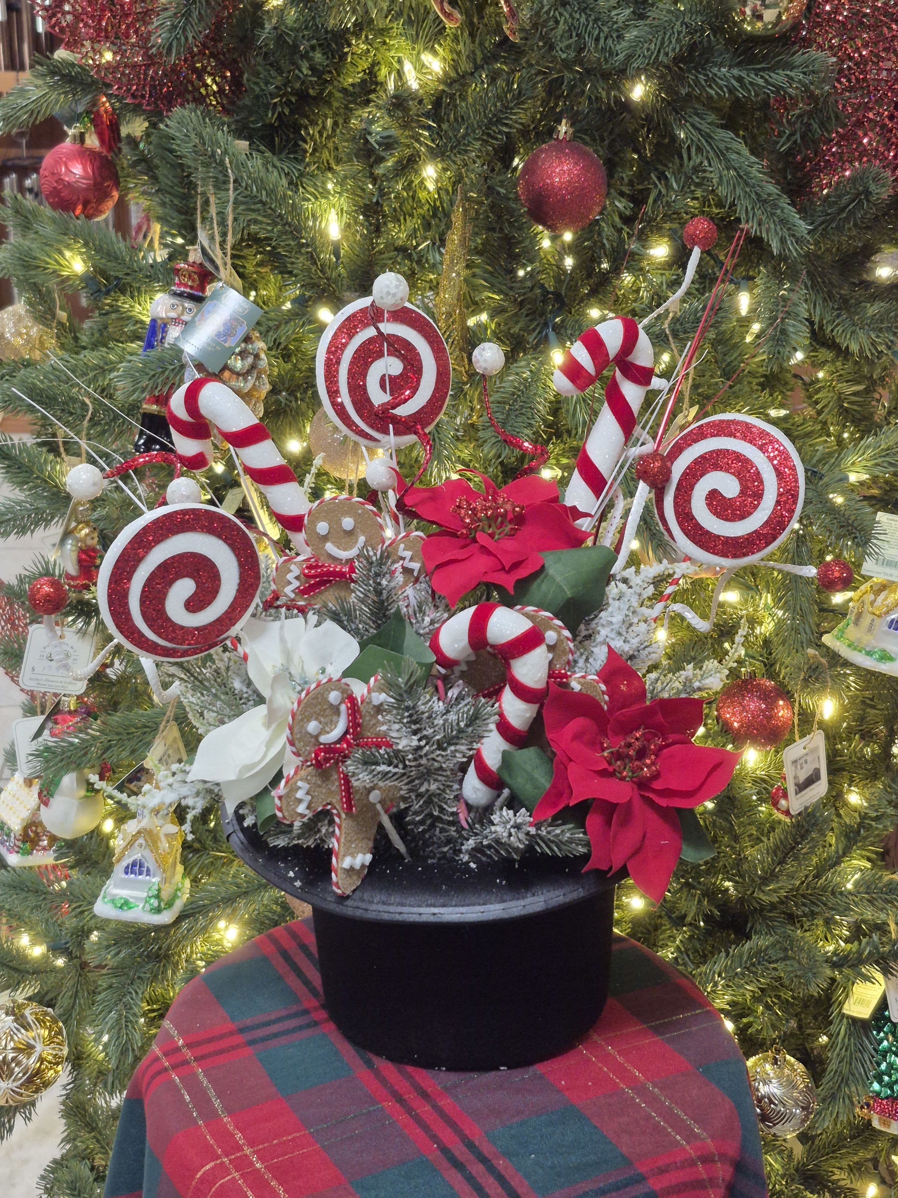 Christmas arrangement with candy canes, gingerbread figures, and red poinsettias in a black hat box