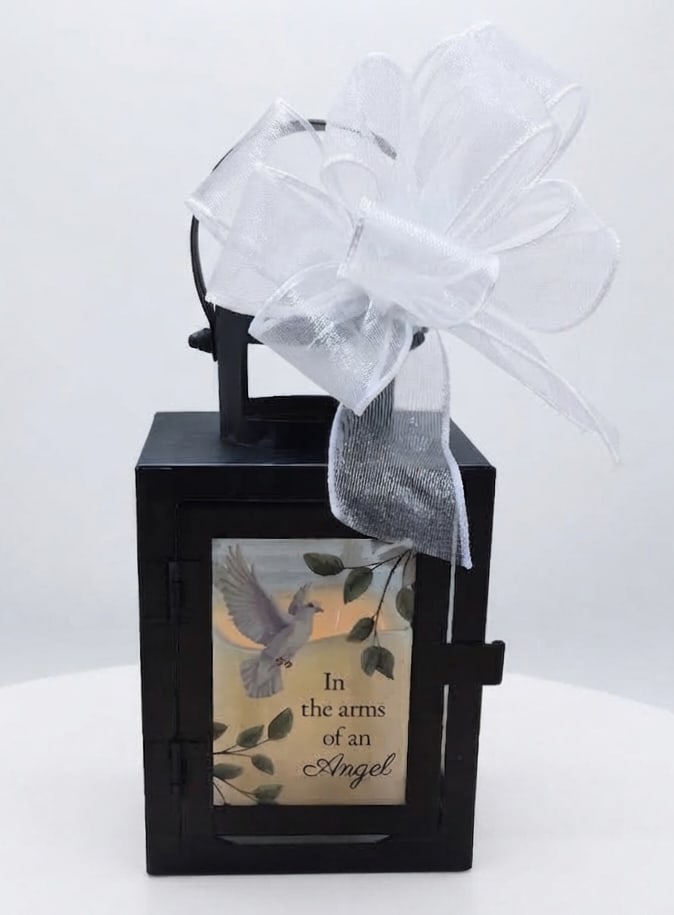 Black lantern with a white bow and memorial plaque reading "In the arms of an Angel"