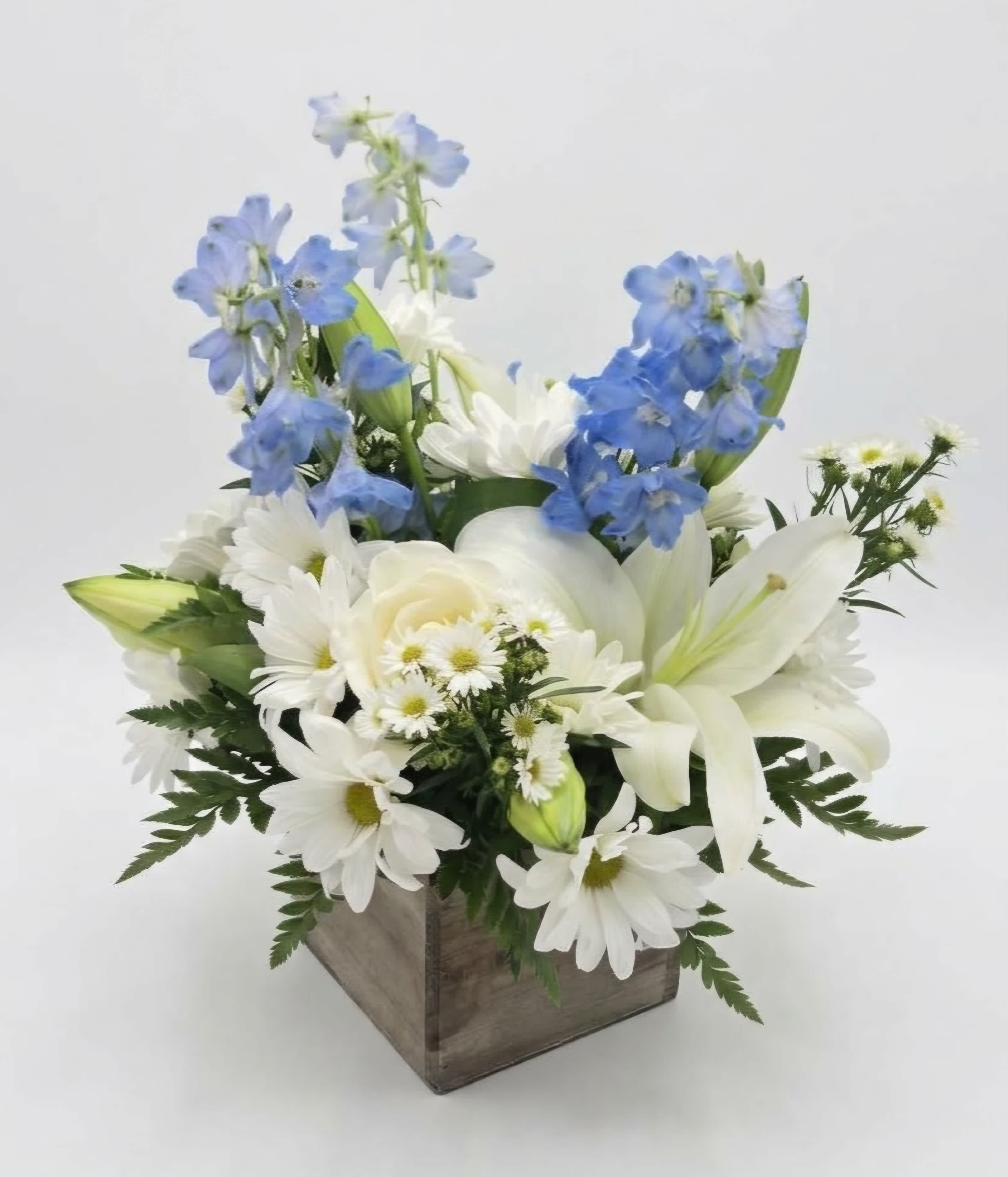 White daisies and lilies with blue delphinium in a wooden box