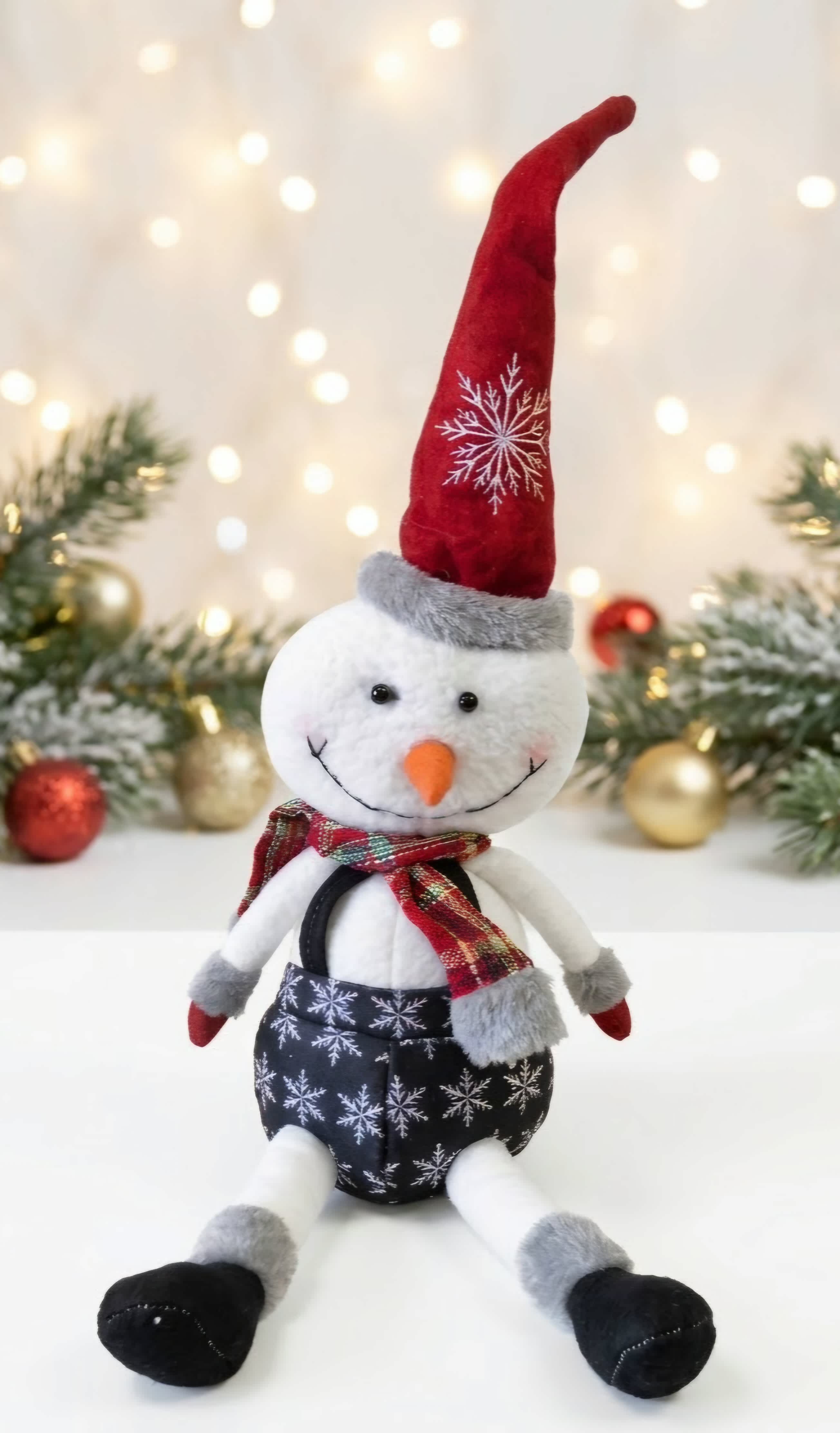 Plush snowman in a red hat and scarf with Christmas decor behind it
