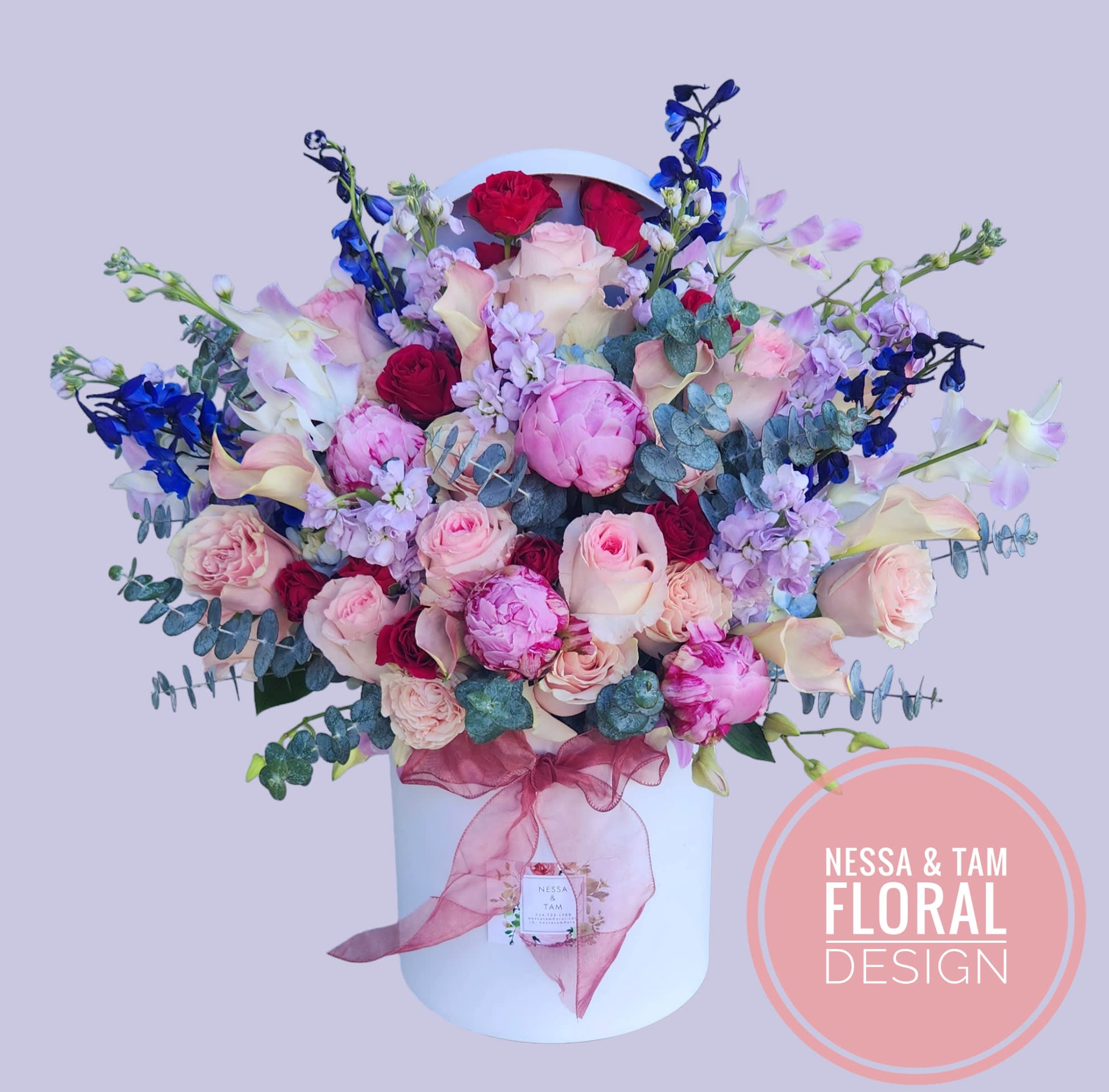 Bouquet of pink and red roses with blue flowers in a white hatbox