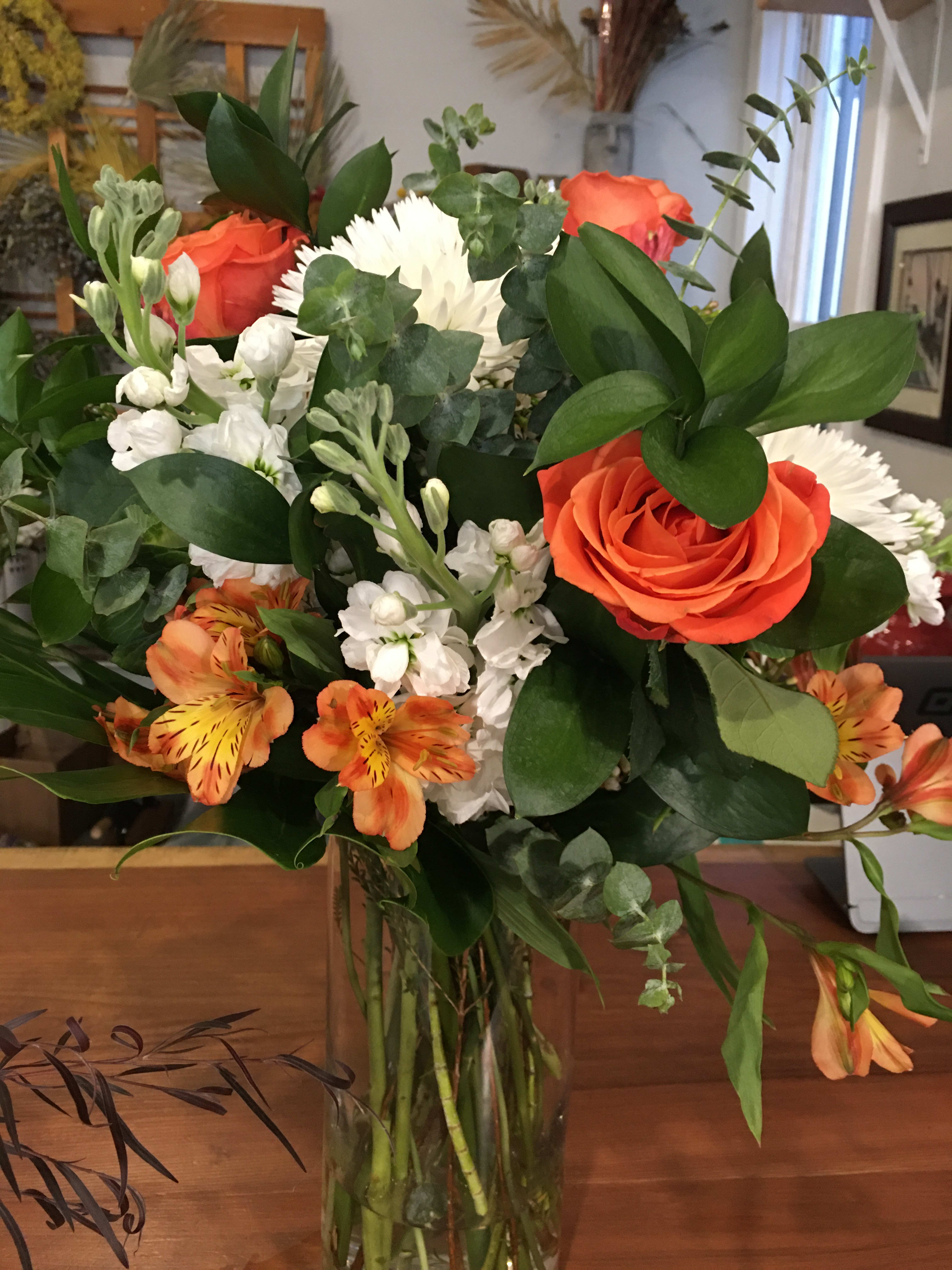 Bouquet of orange roses, white flowers, and orange alstroemeria in a glass vase