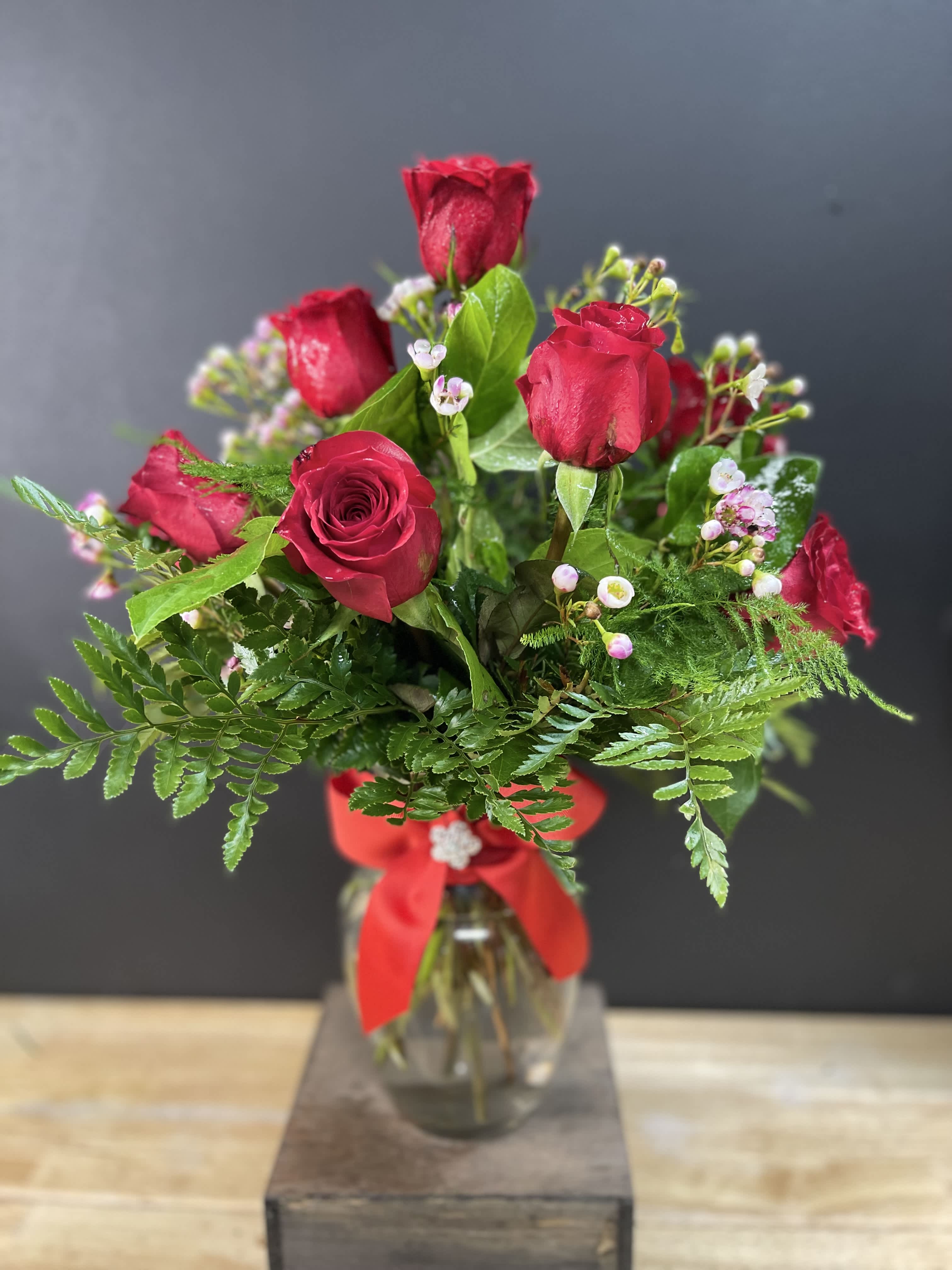 Red roses arranged in a glass vase with a red ribbon