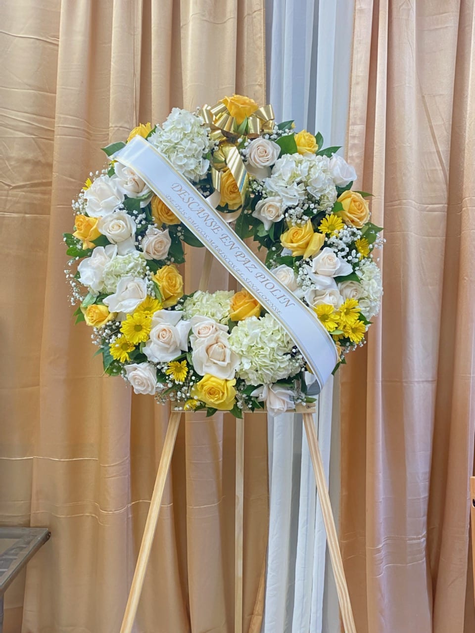 White and yellow floral wreath on a stand with a ribbon