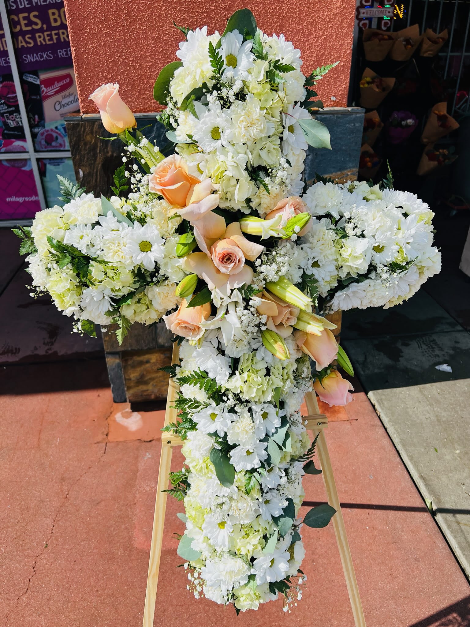Large white floral cross with peach roses on a stand