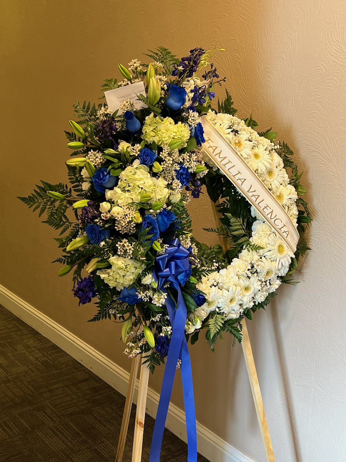 Large funeral wreath of white and blue flowers on a wooden easel