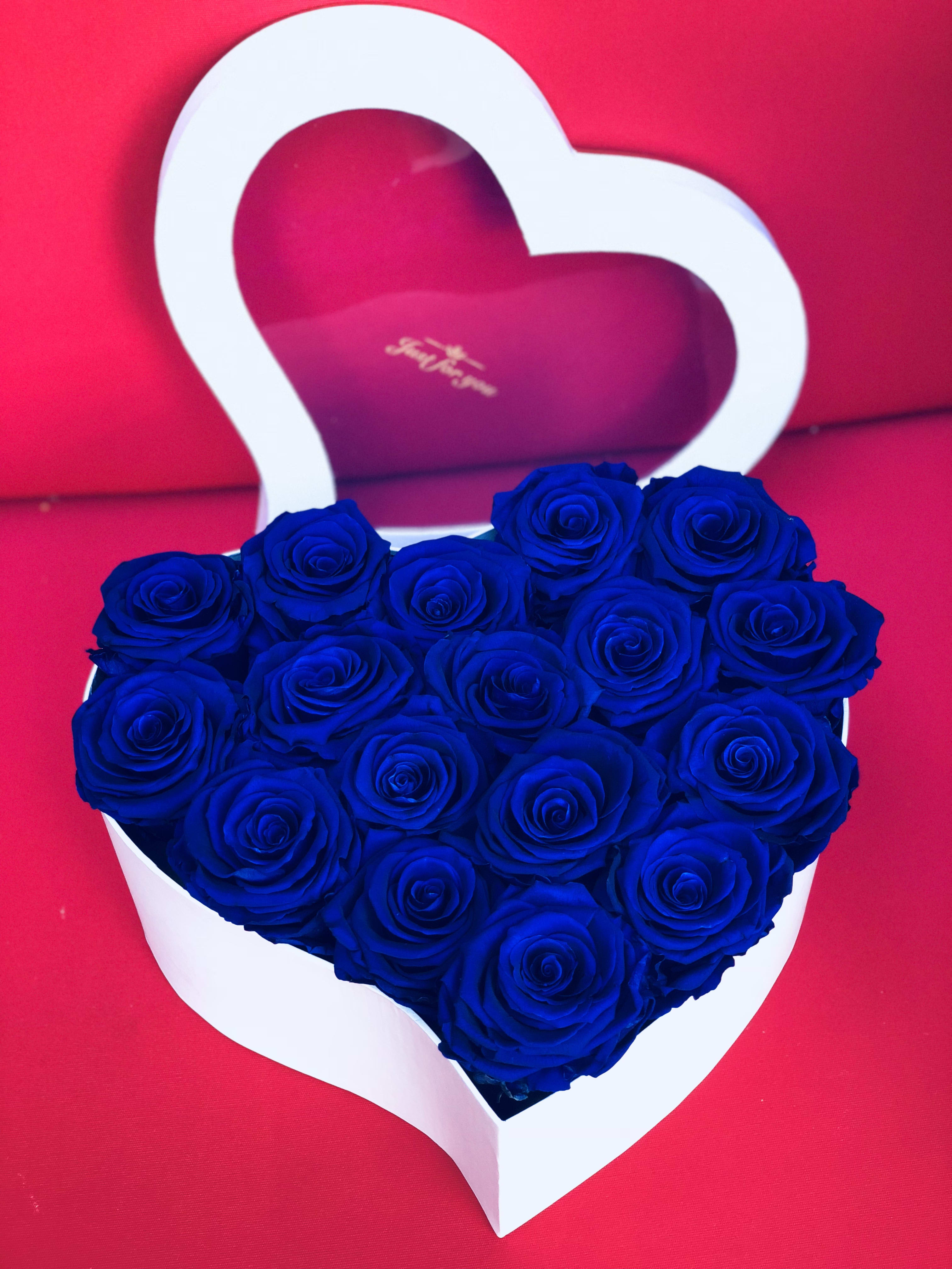 Heart-shaped box of blue roses on a pink background