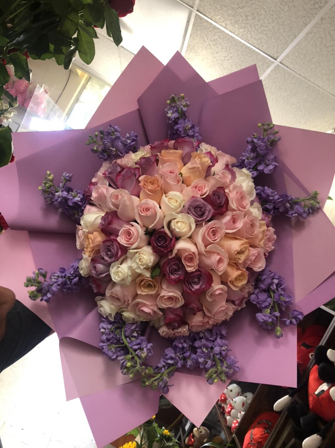 Large bouquet of pastel roses wrapped in pink paper with purple accents