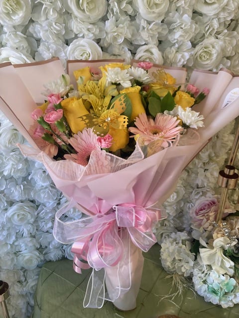 Pink-wrapped bouquet with yellow and pink flowers and a ribbon bow