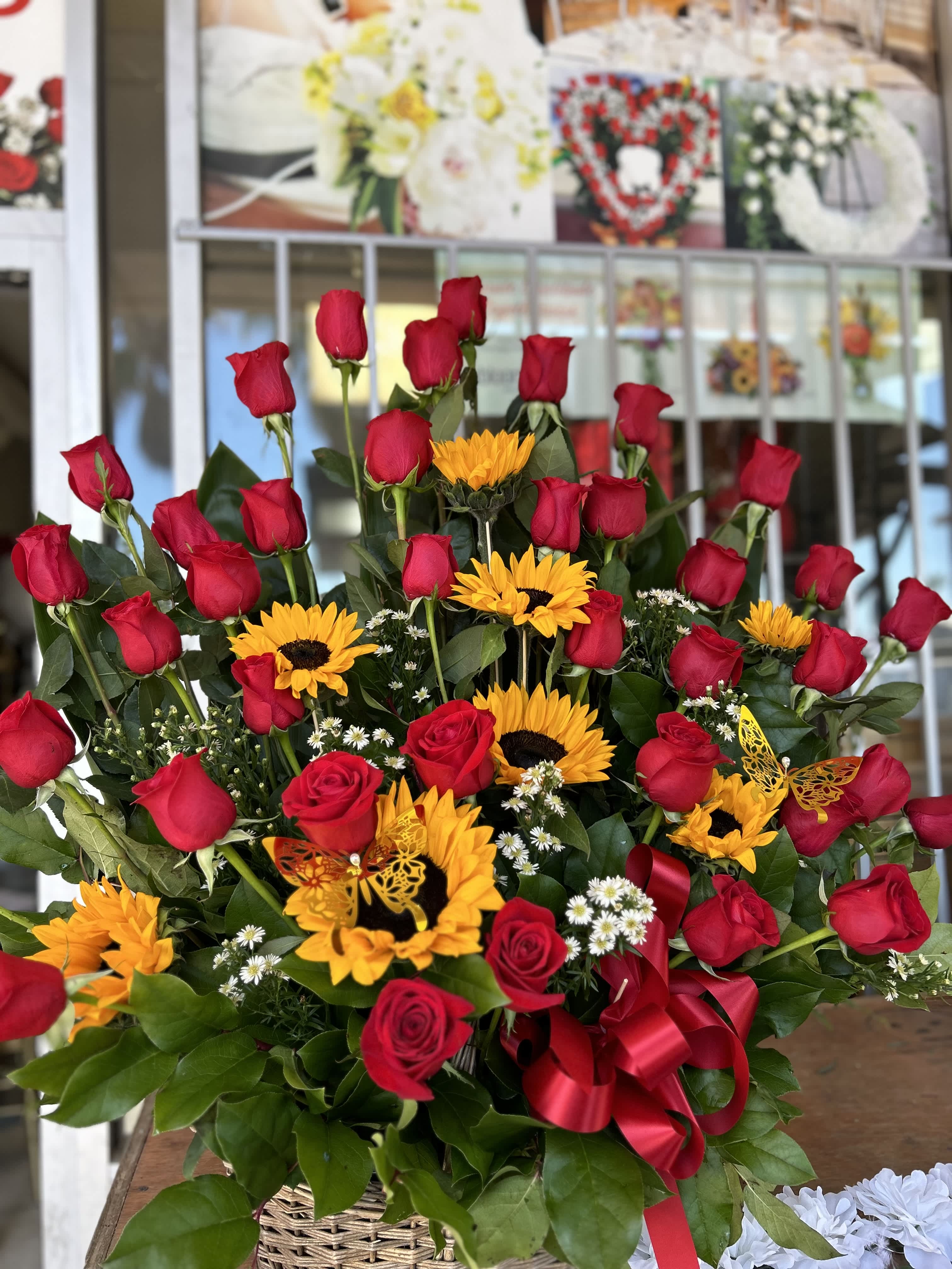 Basket arrangement of red roses and yellow sunflowers with a red ribbon