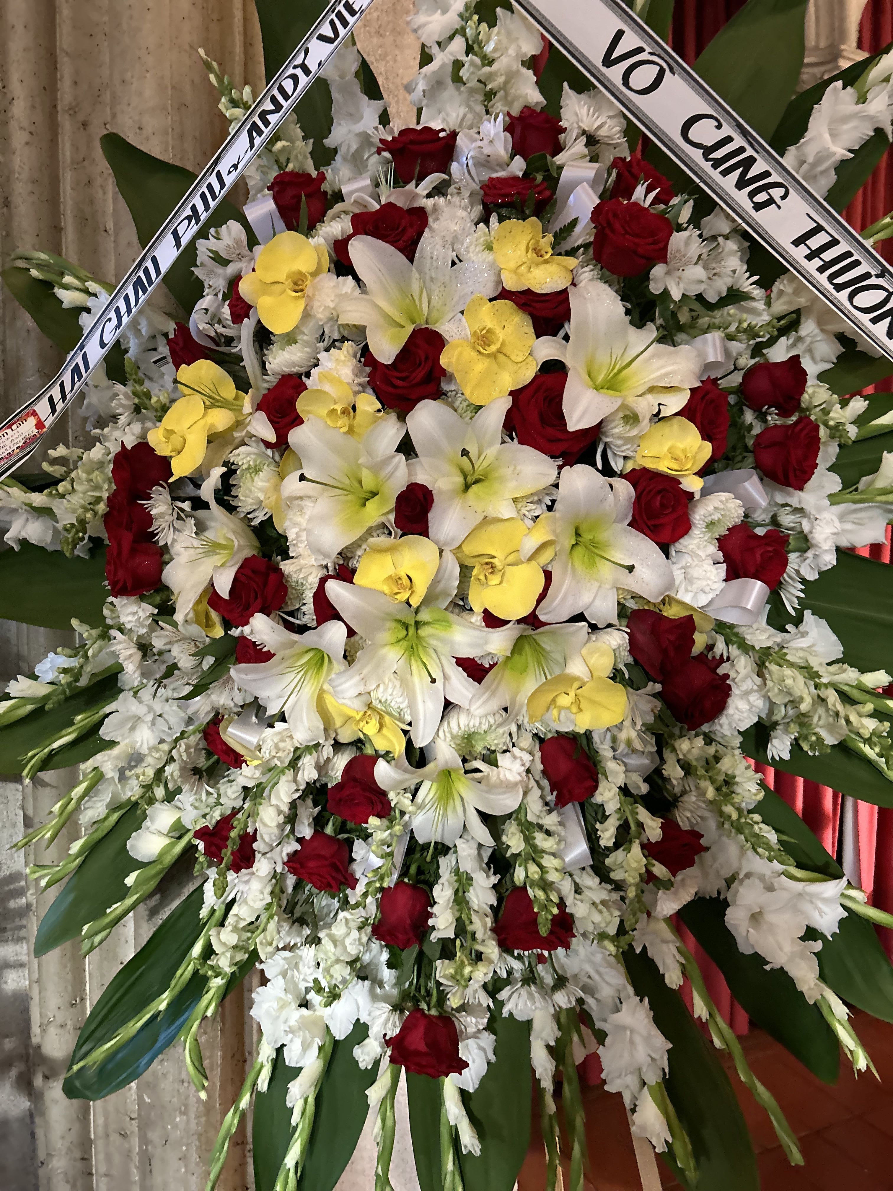 Large funeral wreath of red roses, white lilies, and yellow orchids