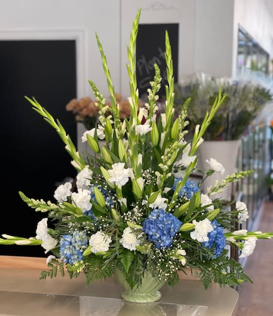 Tall blue and white floral arrangement in a pale green vase