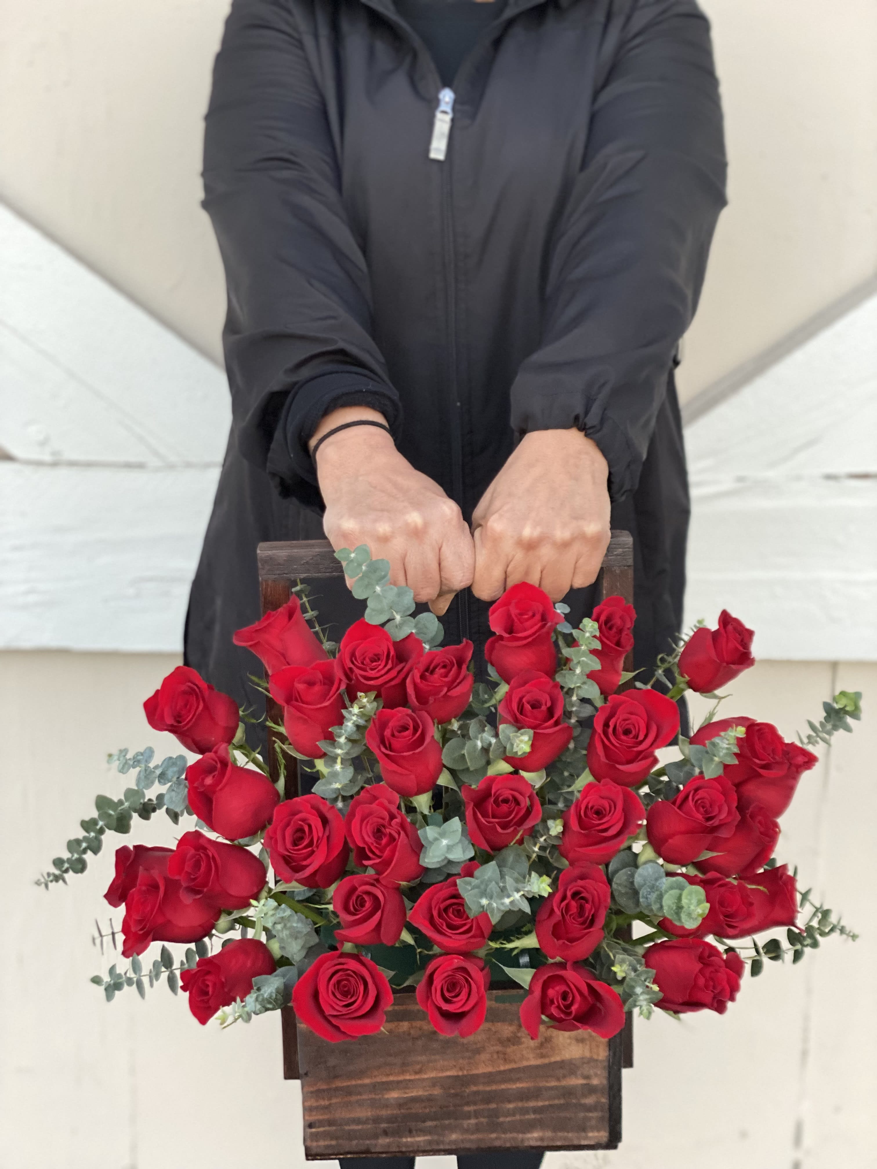 Handheld wooden box filled with red roses and eucalyptus