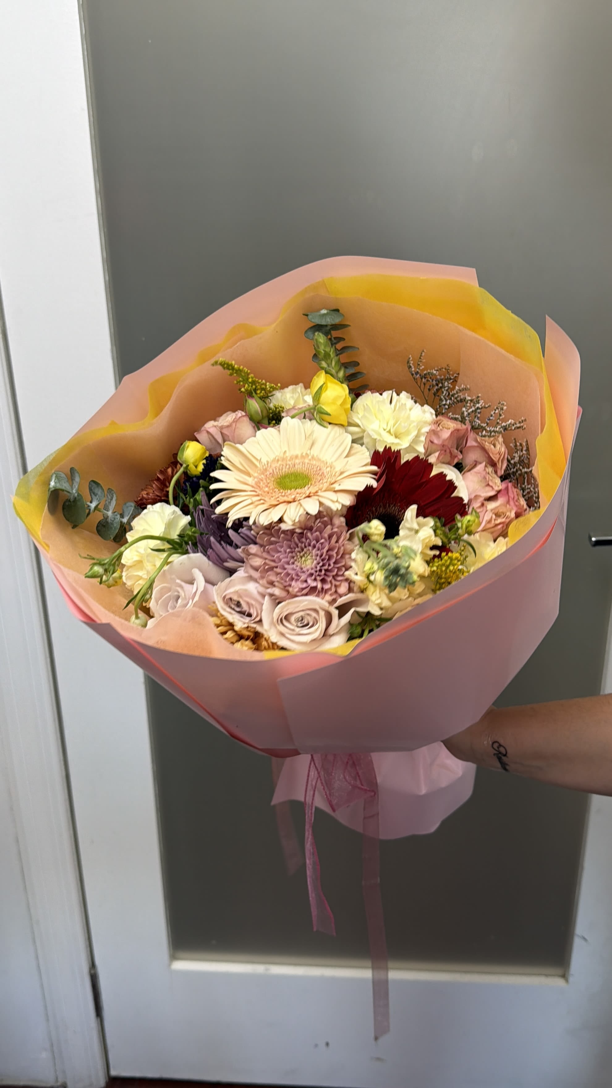 Hand-tied bouquet of mixed pastel flowers wrapped in pink and peach paper