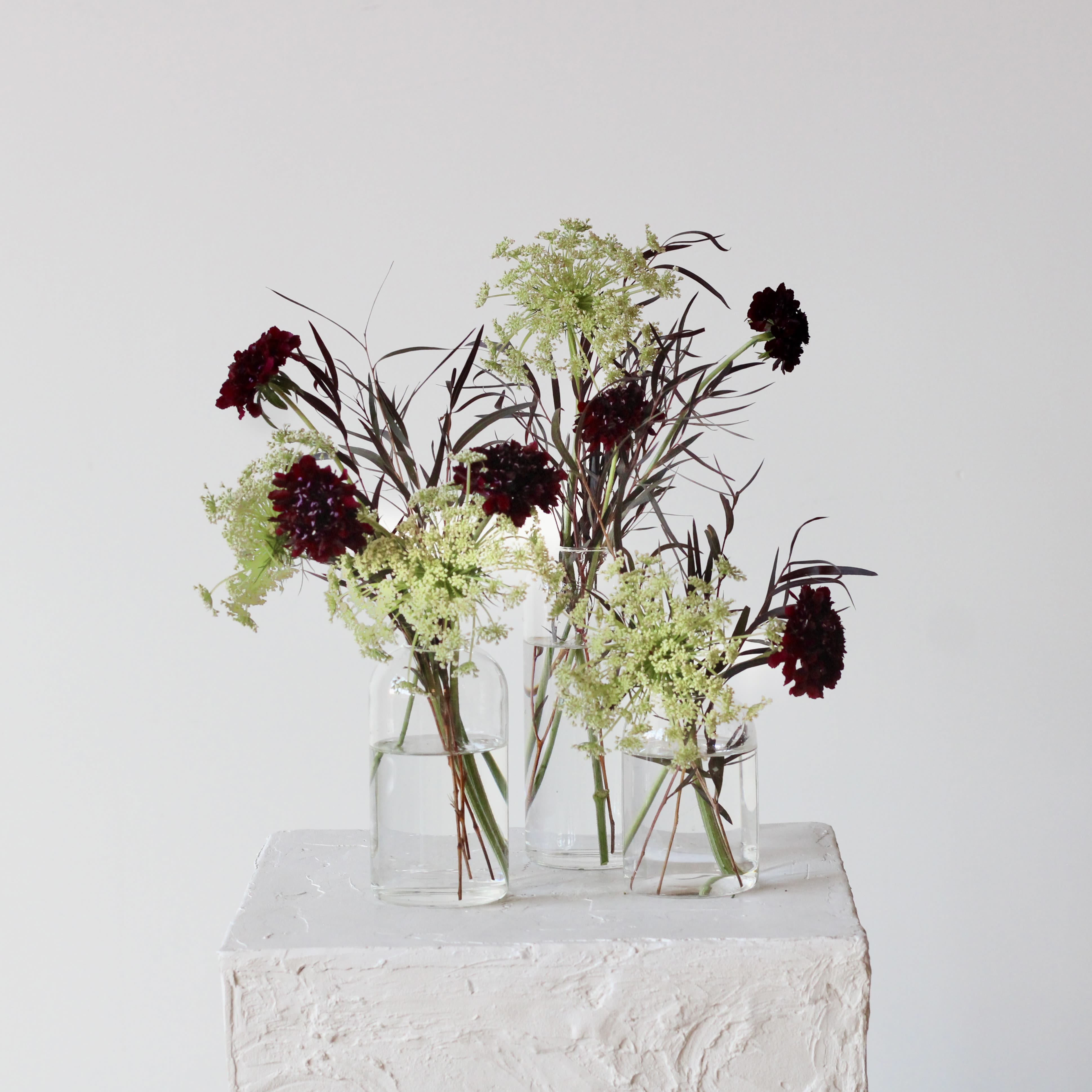 Three small glass vases hold dark red flowers with airy white filler.