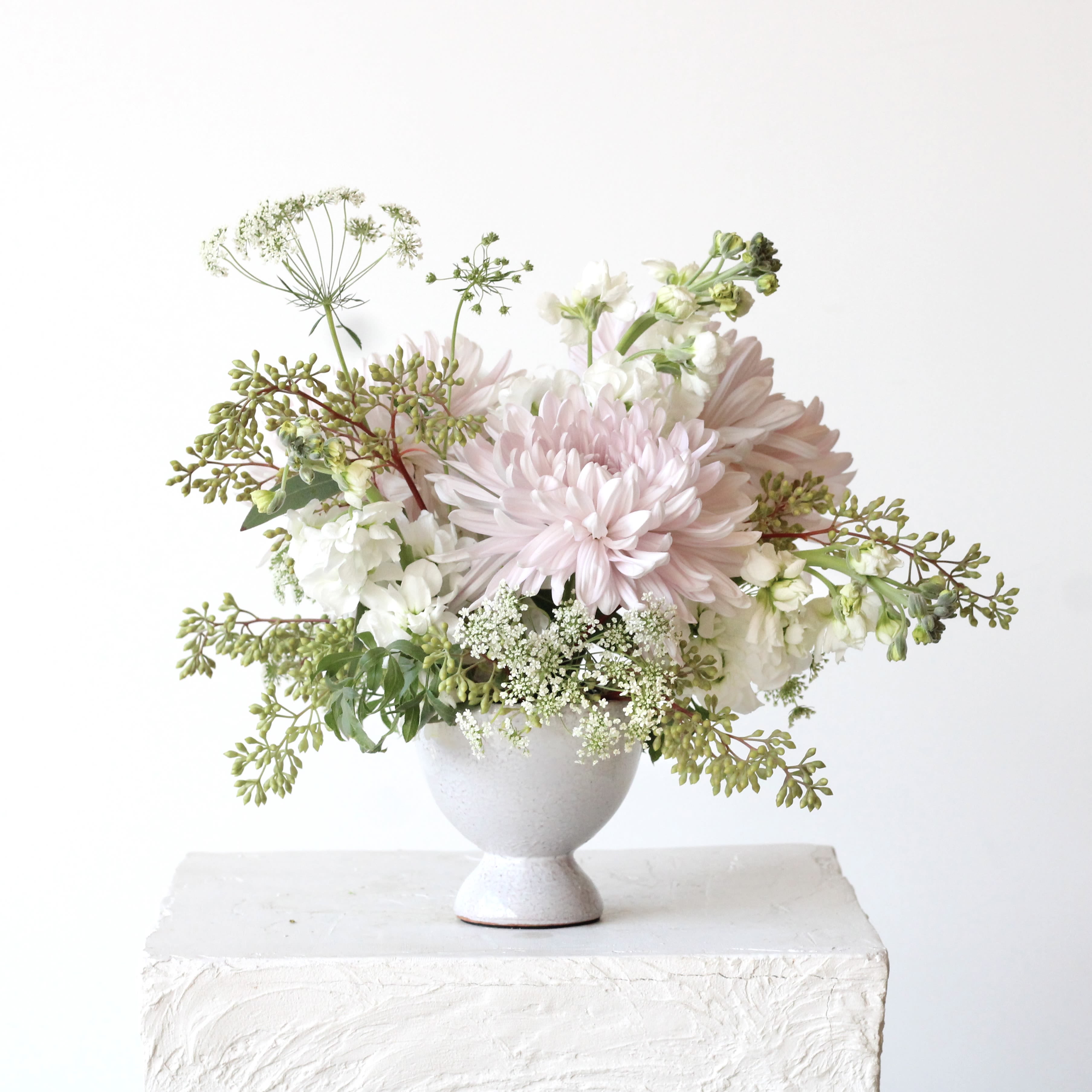 Soft pink and white flowers arranged in a white pedestal vase