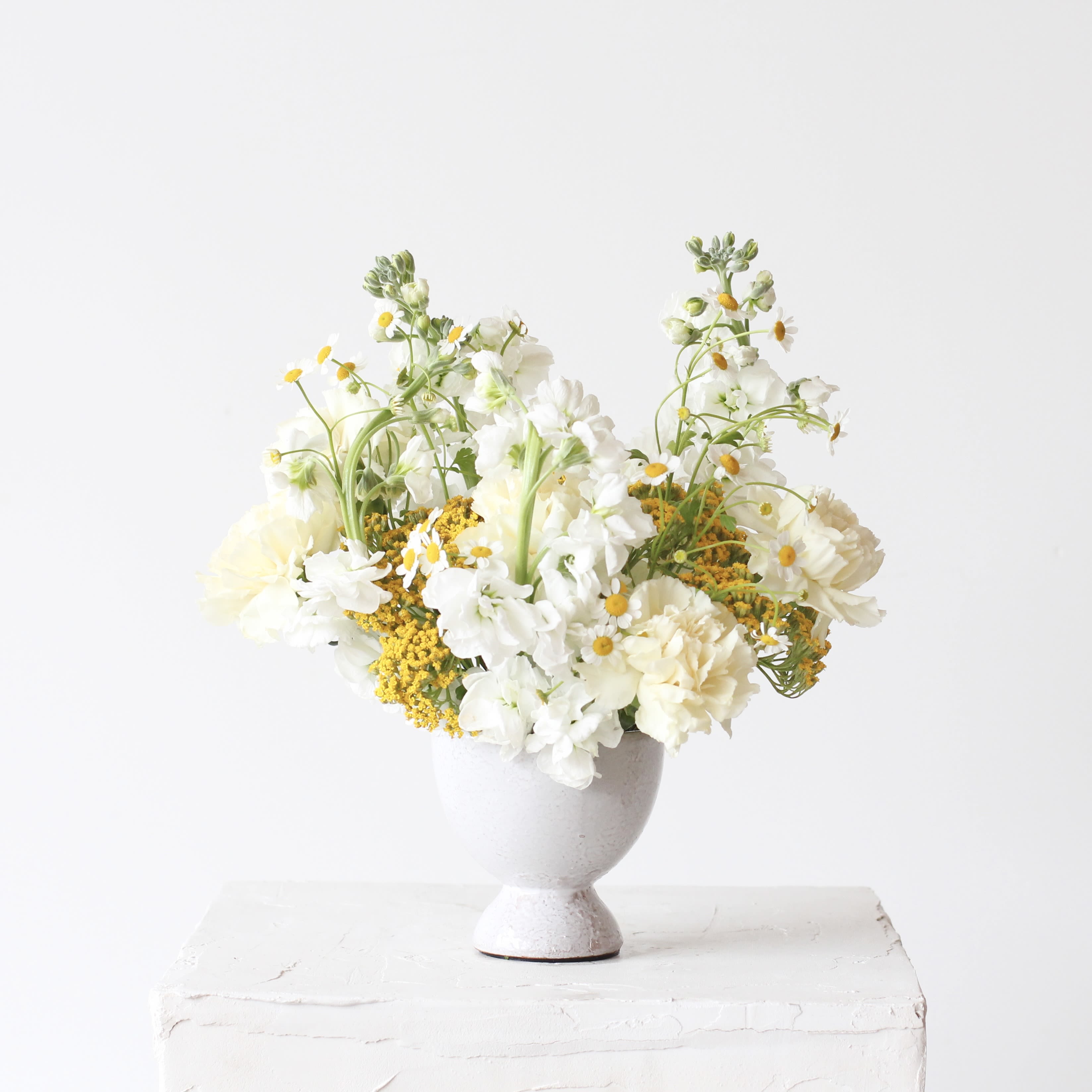 White and pale yellow flowers arranged in a gray pedestal vase