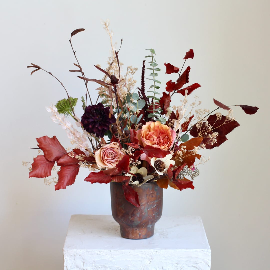 Autumn floral arrangement in a copper-toned vase with red and peach blooms