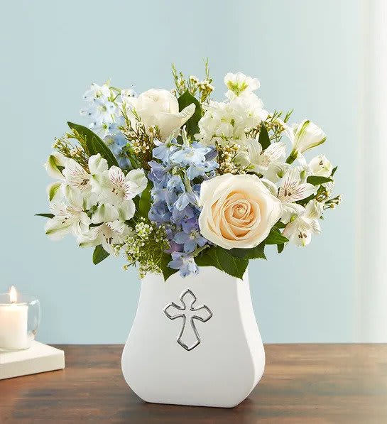White and cream roses with blue and white blooms in a white vase with a cross emblem