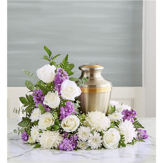 Cremation urn surrounded by white roses, white mums, and purple flowers in a crescent arrangement