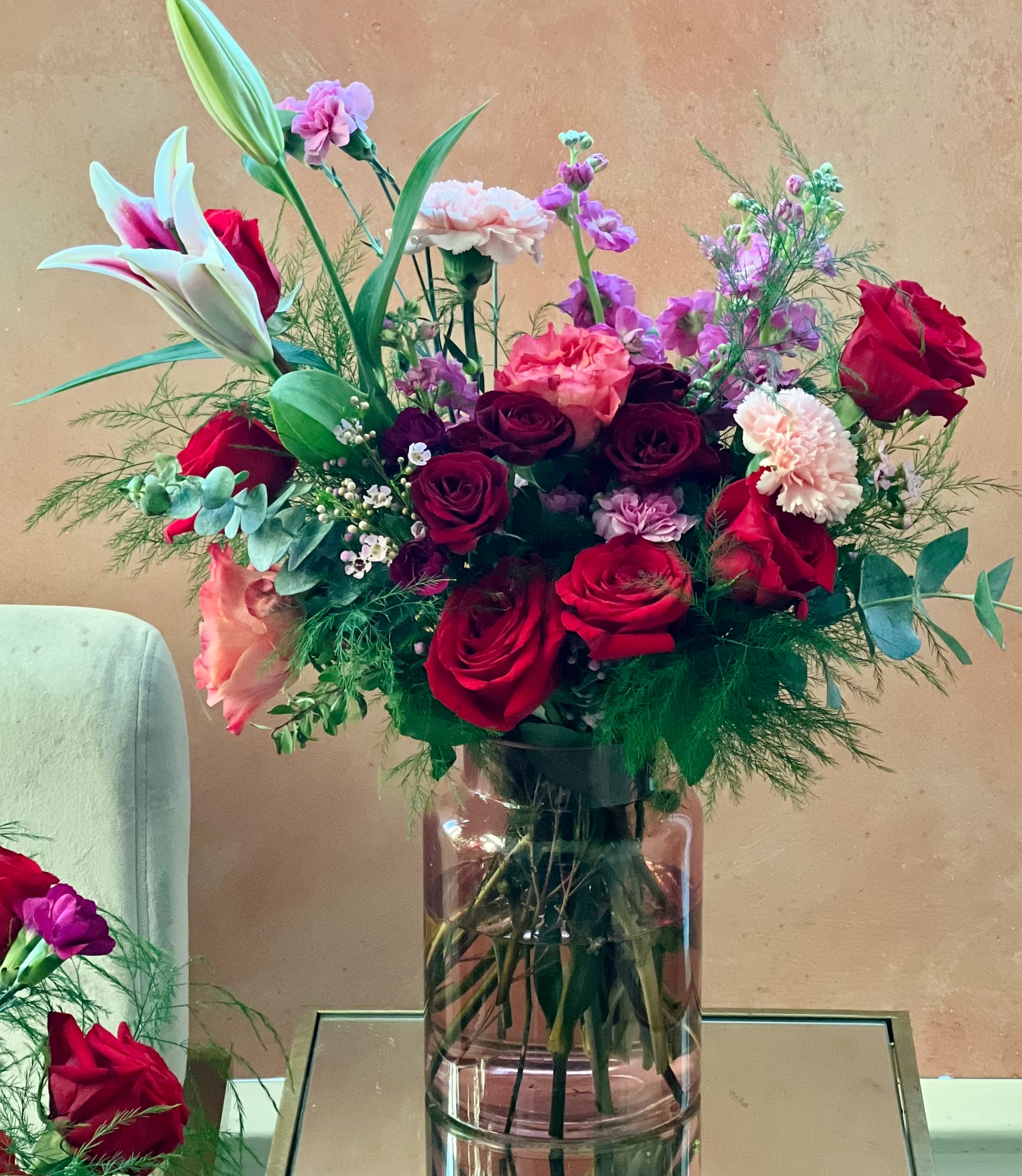 Mixed bouquet of red roses, lilies, and pink carnations in a glass vase