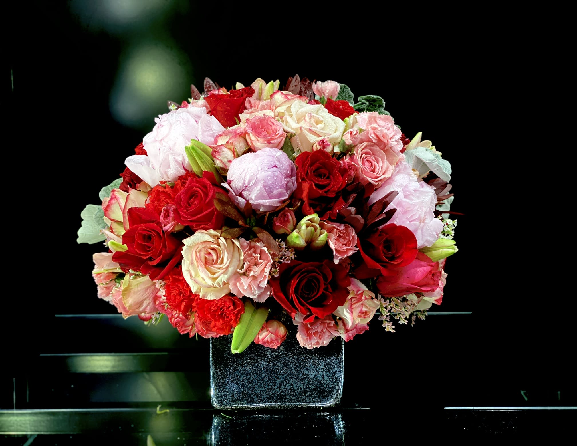 Bouquet of red, pink, and white roses in a square vase