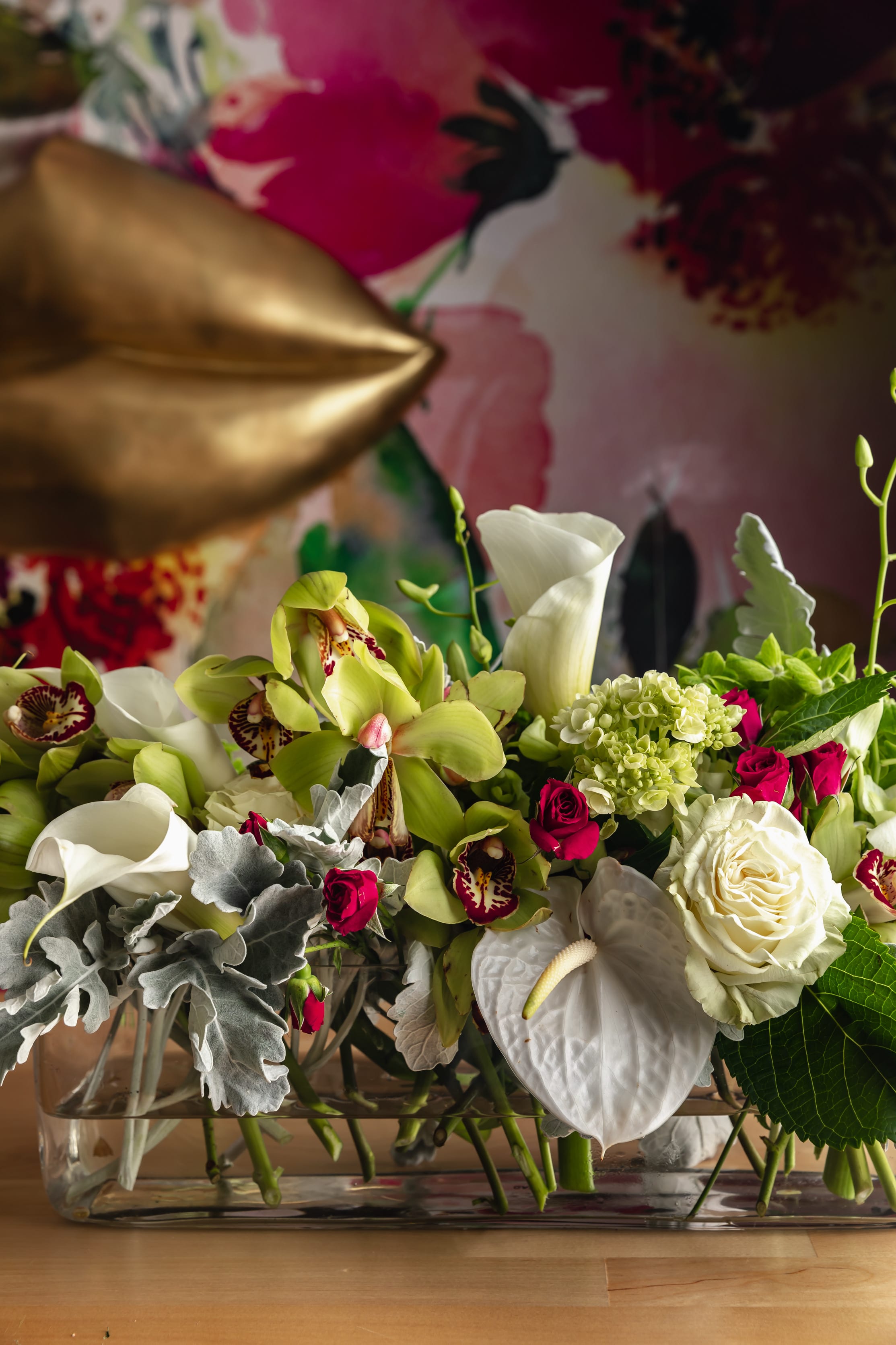 Mixed floral arrangement in a glass vase with white calla lilies, roses, and orchids