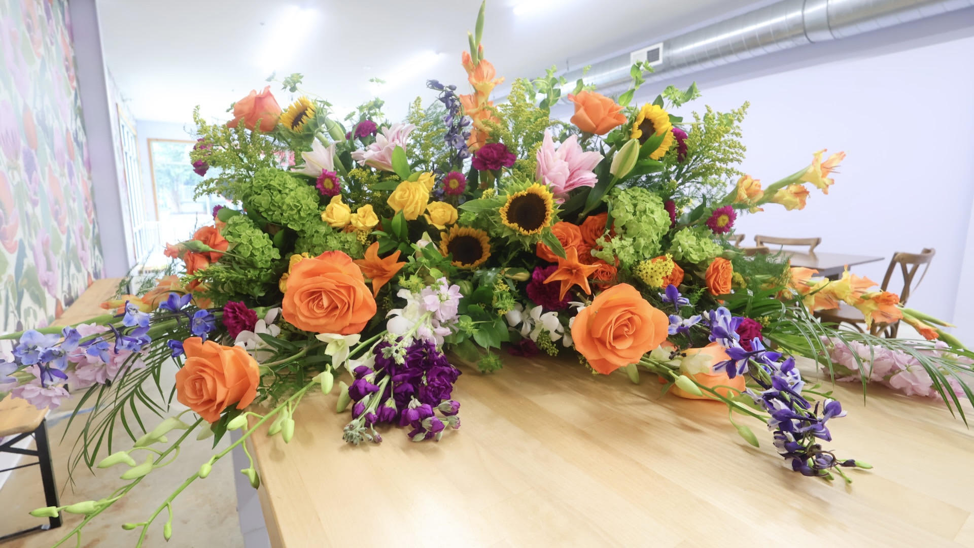 Large mixed floral arrangement with orange roses, sunflowers, and lilies on a table